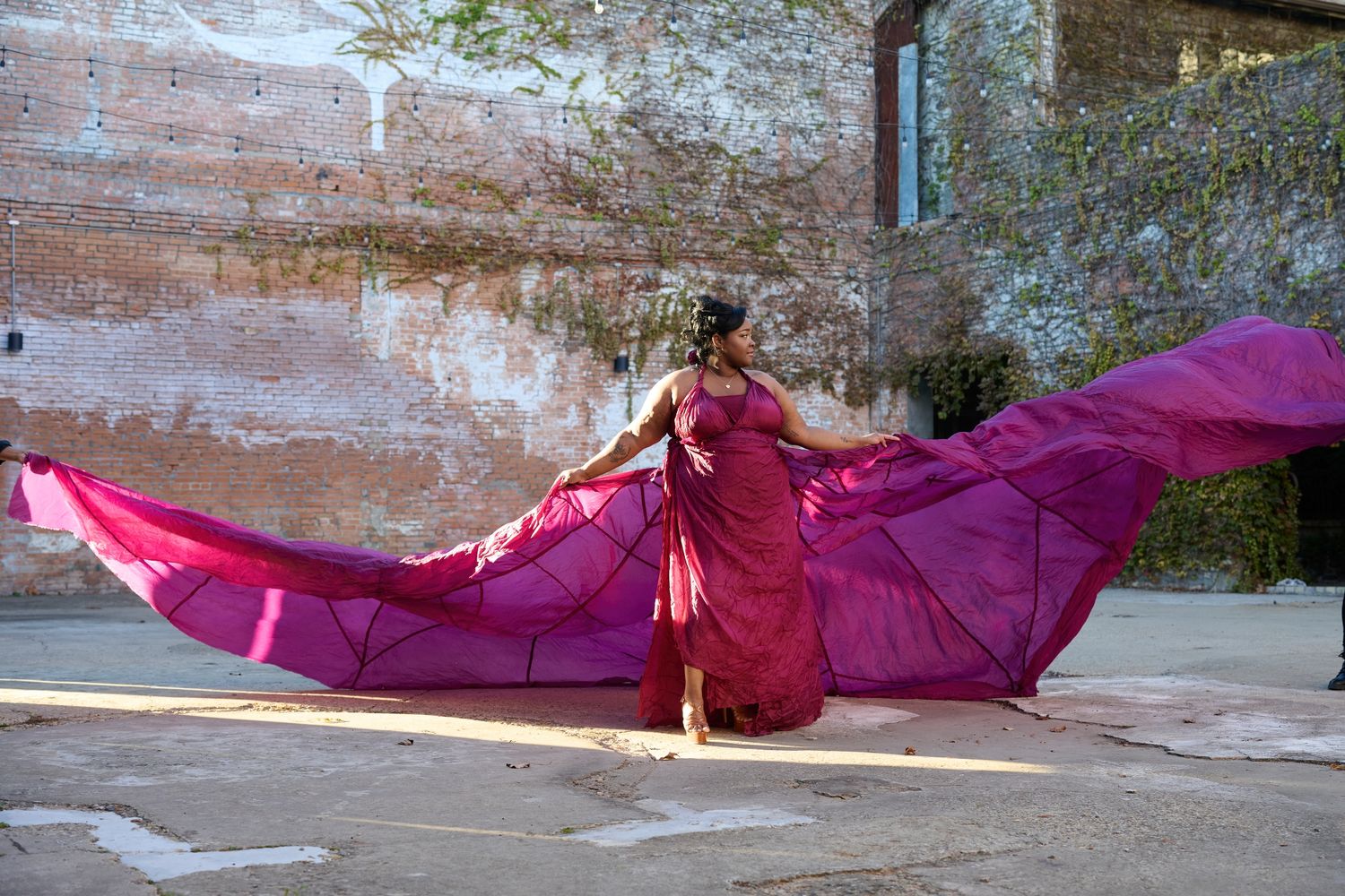 Flowing magenta fabric draped dramatically against weathered wall backdrop.