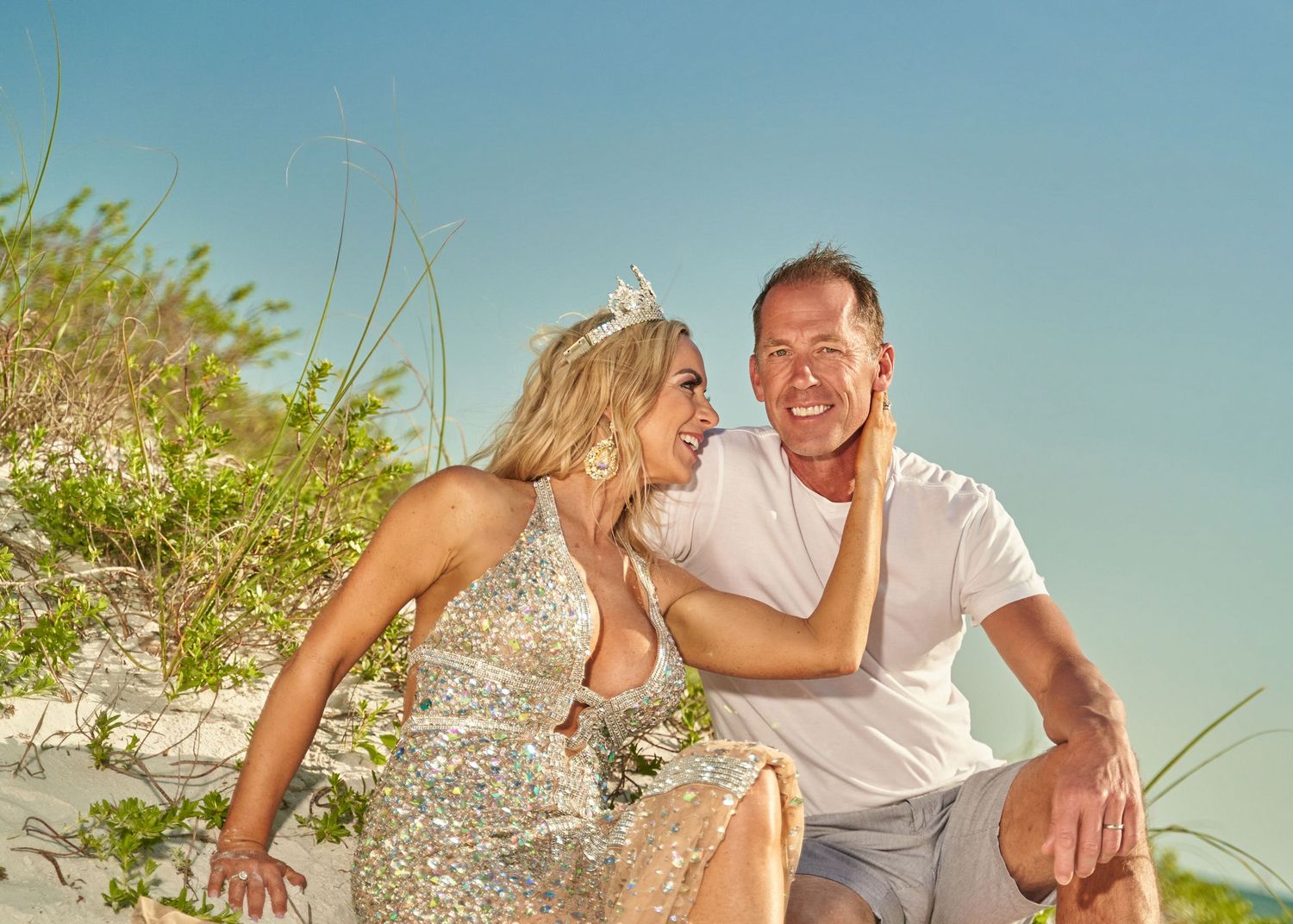 Playful couple posing on sandy beach dunes during a sunny afternoon.