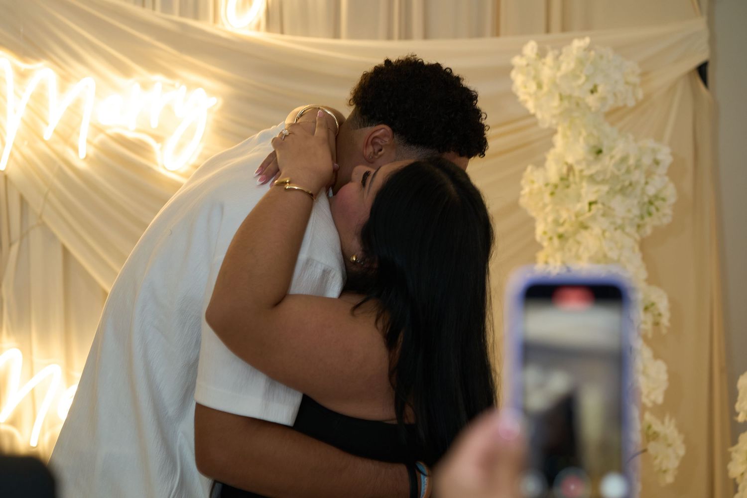 A romantic embrace captured at an elegant event with white floral decorations and draped fabric.