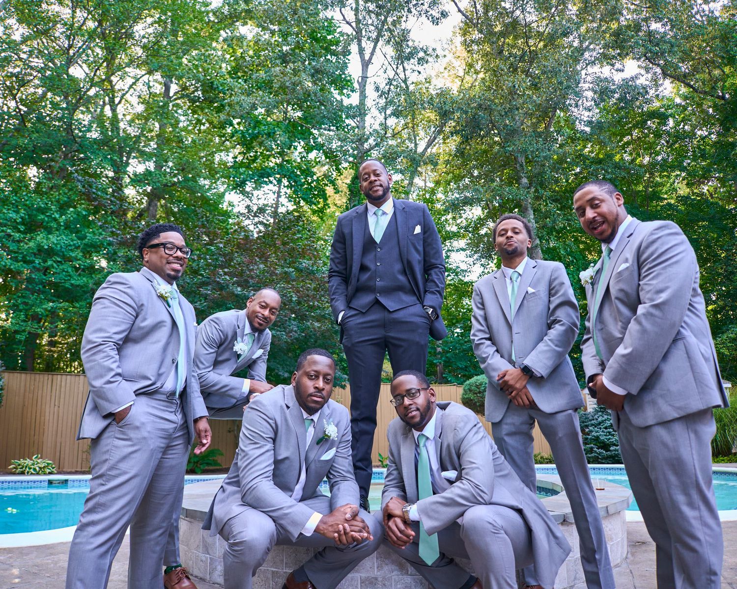 Groomsmen in matching gray suits share candid moments during outdoor wedding photoshoot.