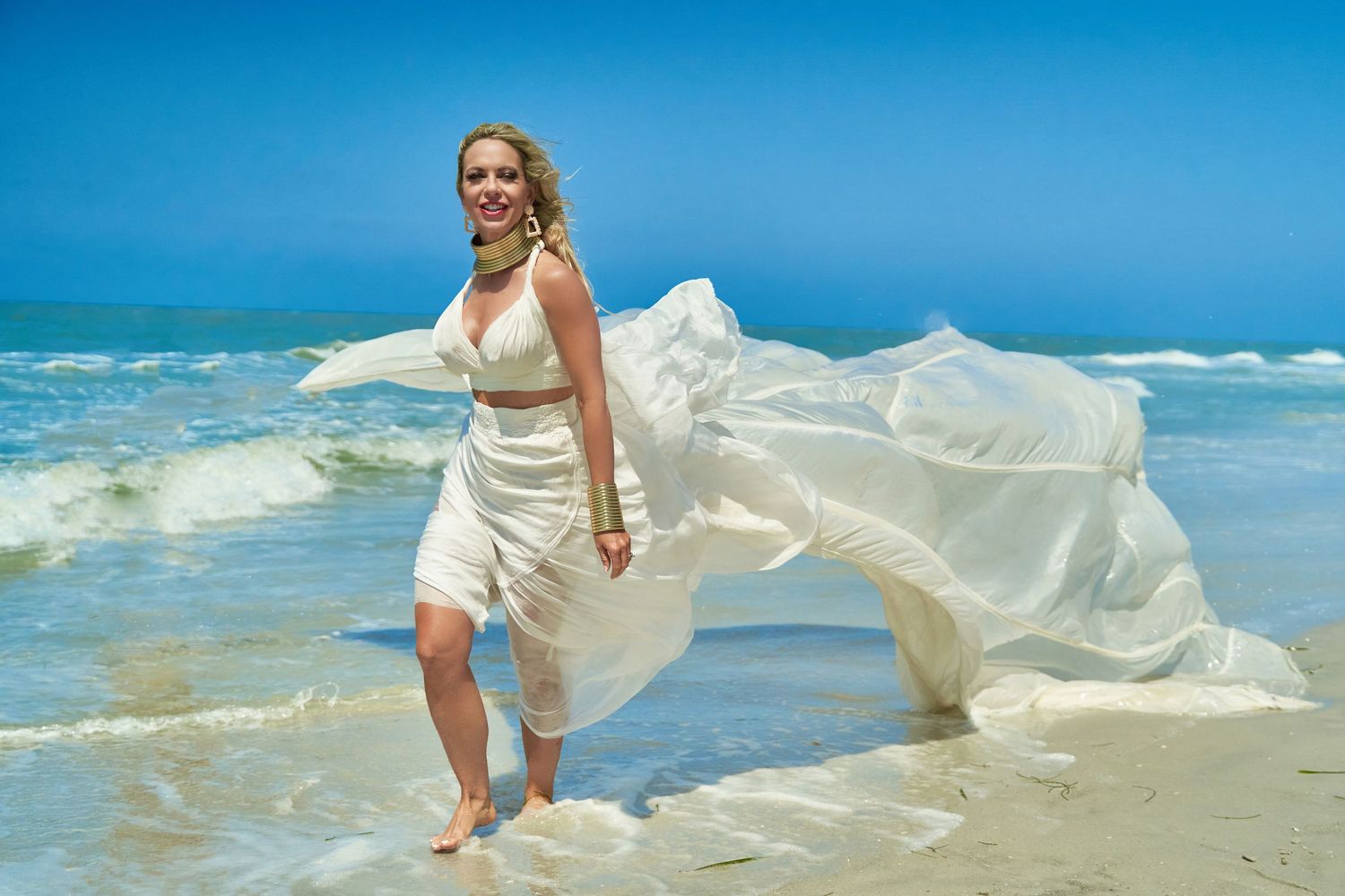 Beach photoshoot series featuring flowing white dress billowing in ocean breeze.