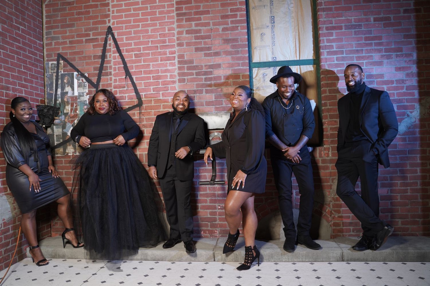 Group photo session against brick wall backdrop in casual dark attire.