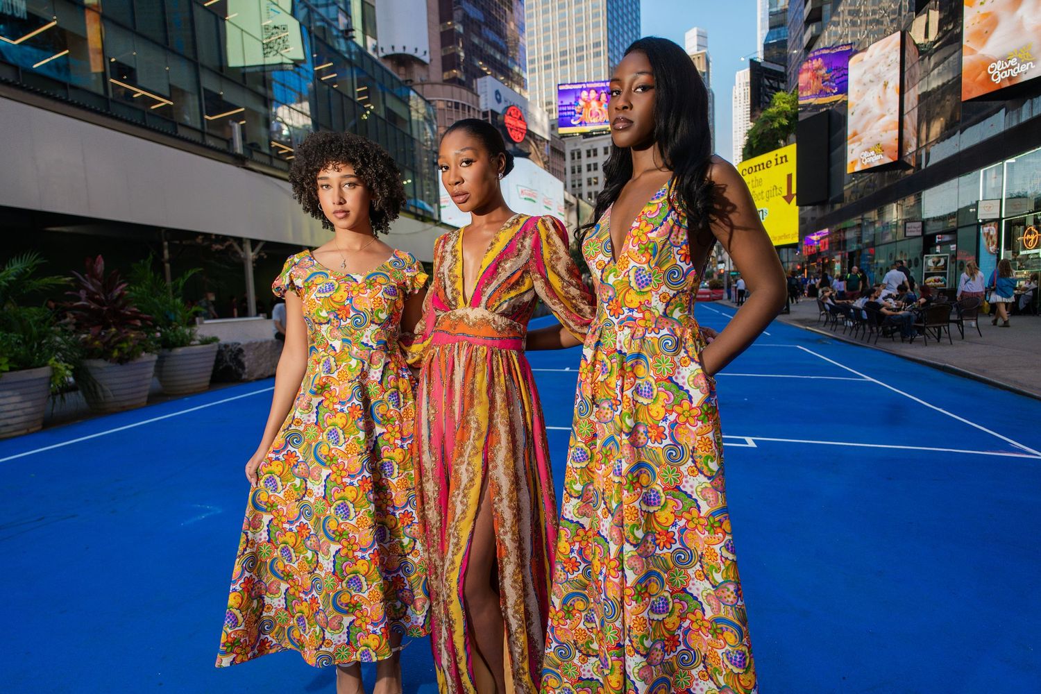 People in colorful floral dresses stand together on a bright blue tennis court surface.
