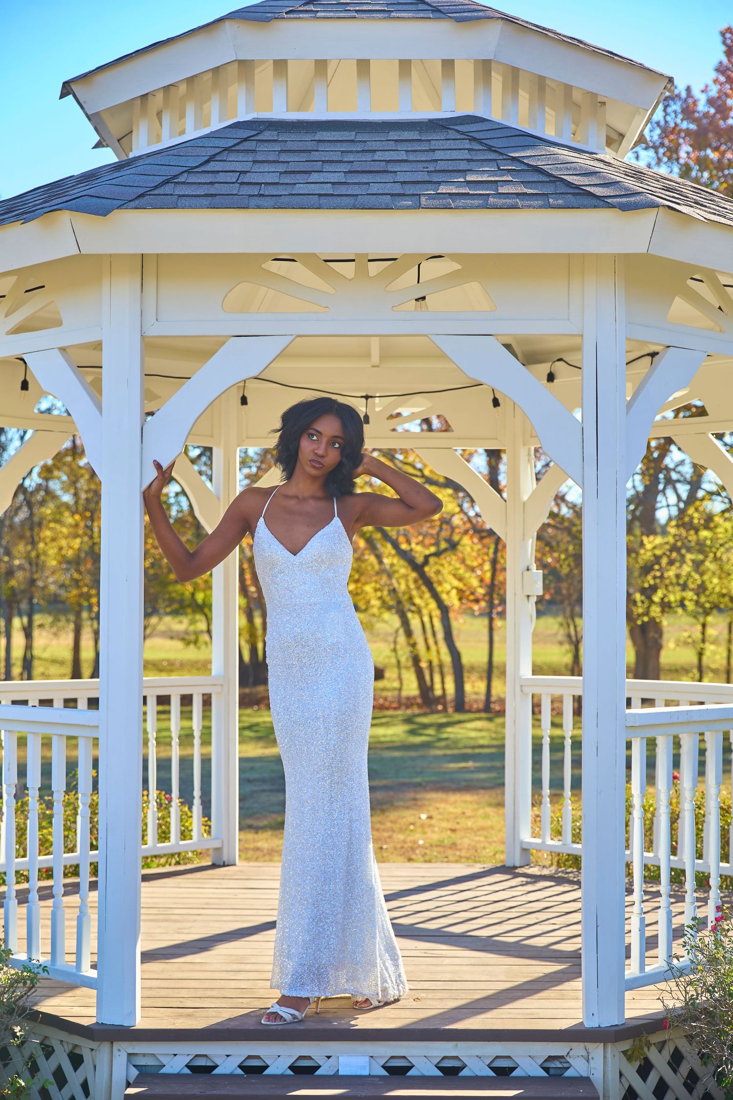 Bride in lace wedding dress posing in white gazebo during golden hour.