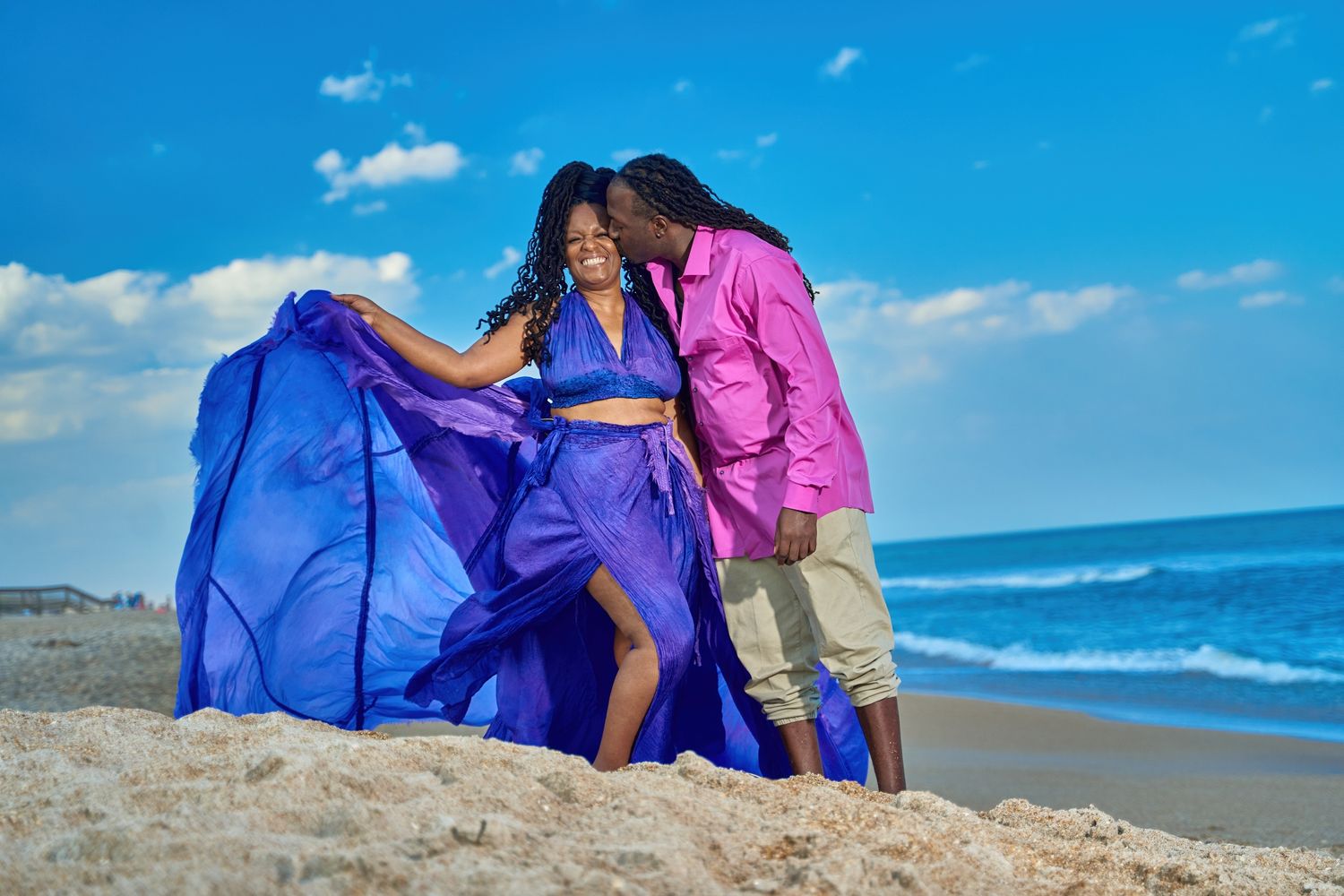 Couple enjoying a romantic moment together on a sunny beach with blue ocean waves in the background.