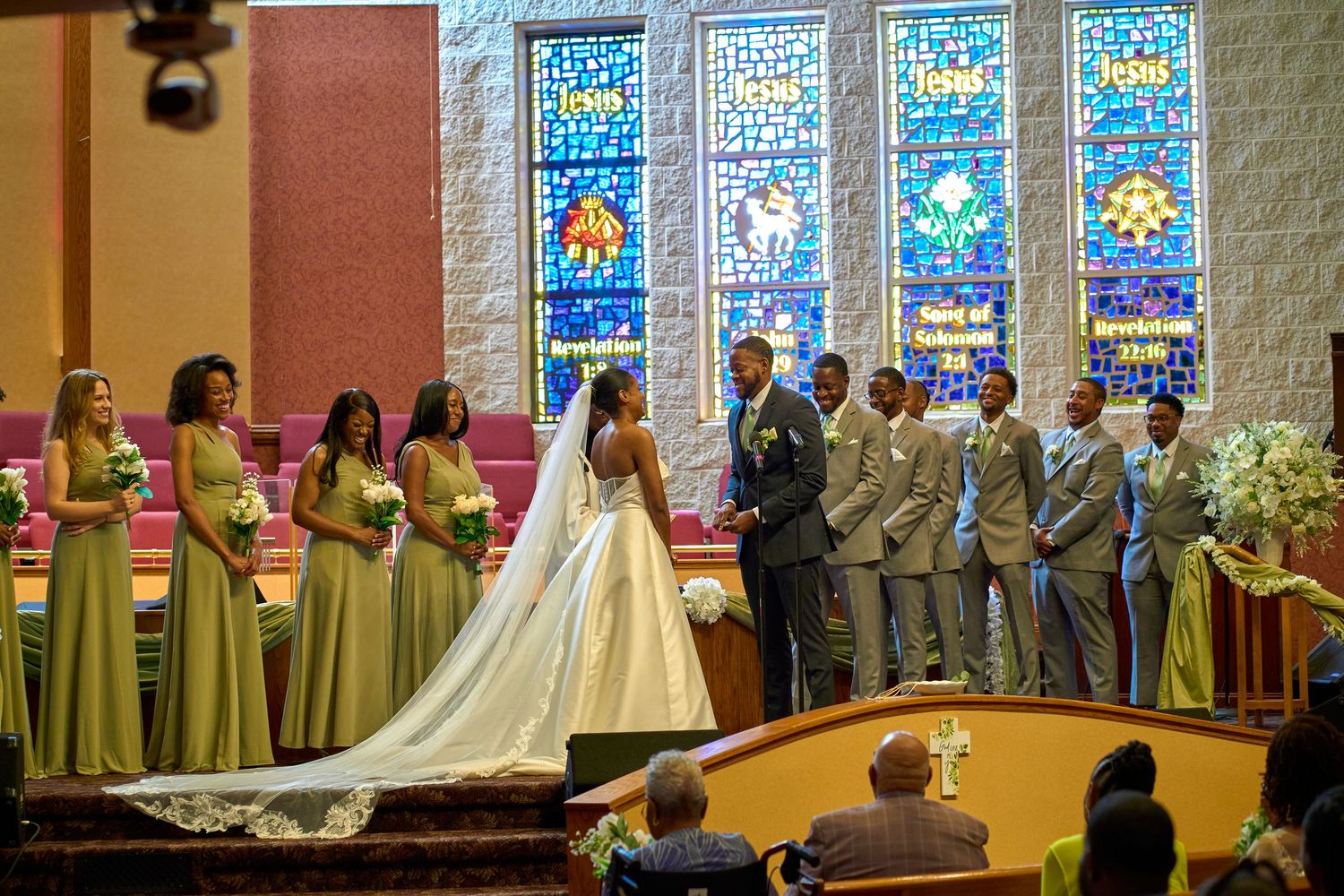 A wedding ceremony in a church with stained glass windows and bridesmaids in lime green dresses.