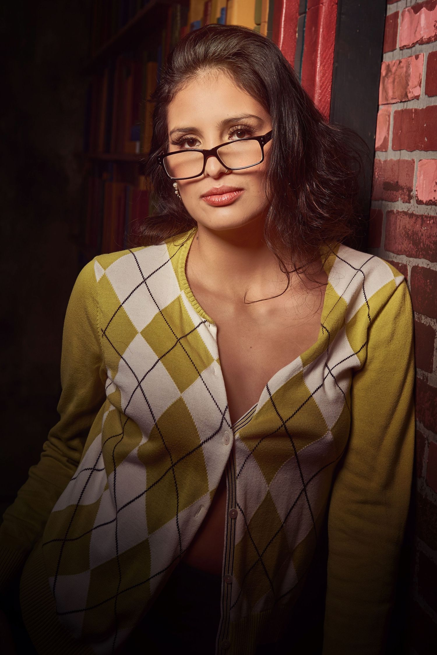 Portrait in yellow argyle sweater and glasses against brick wall background.