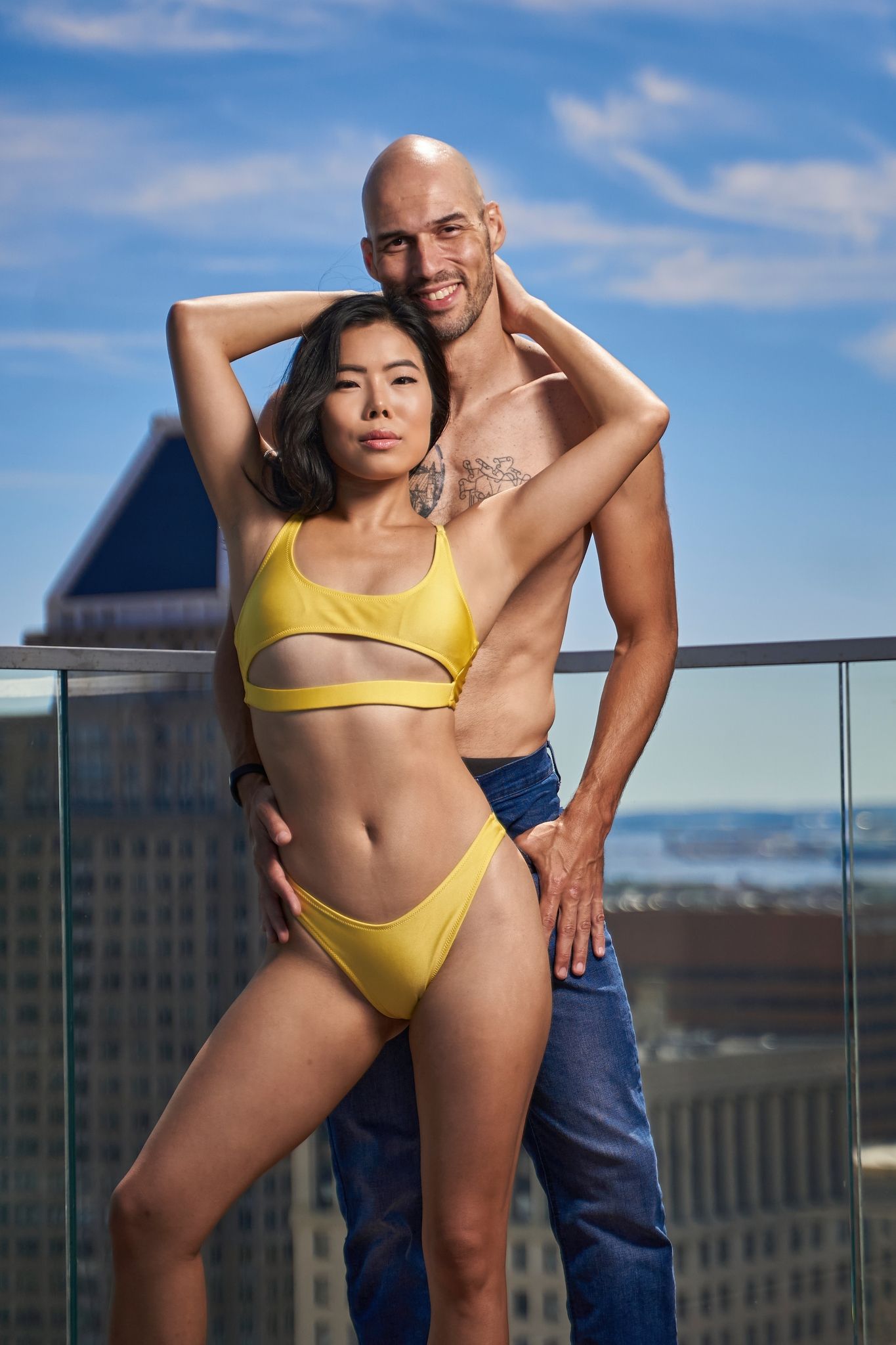 Couple poses on a rooftop terrace with city skyline in the background.