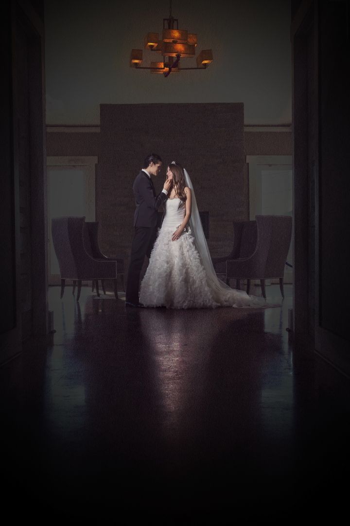 A romantic silhouette of a couple in wedding attire sharing an intimate moment in a dimly lit indoor space.