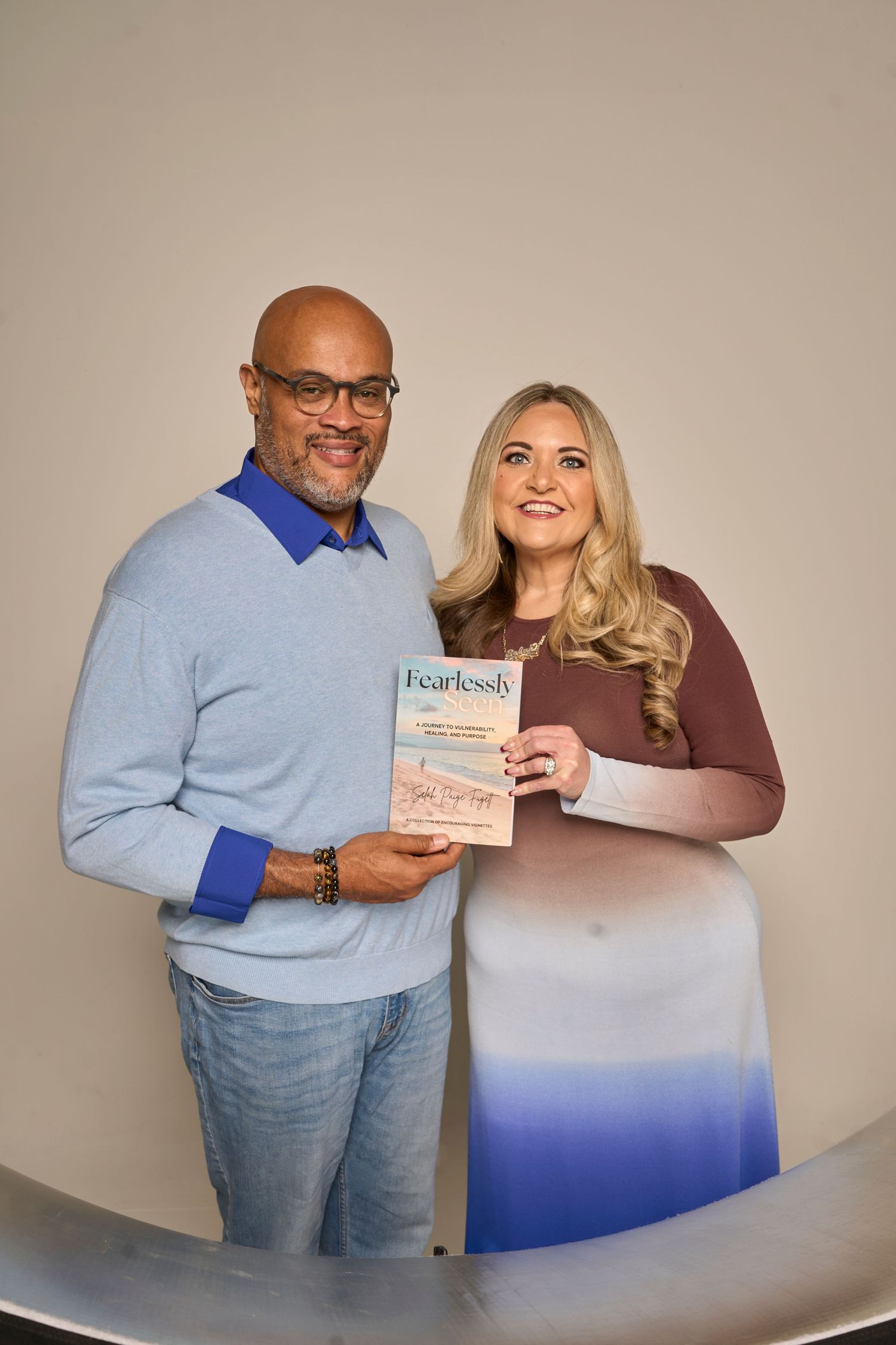 Pair holding books while posing in coordinated blue and brown outfits in studio setting.