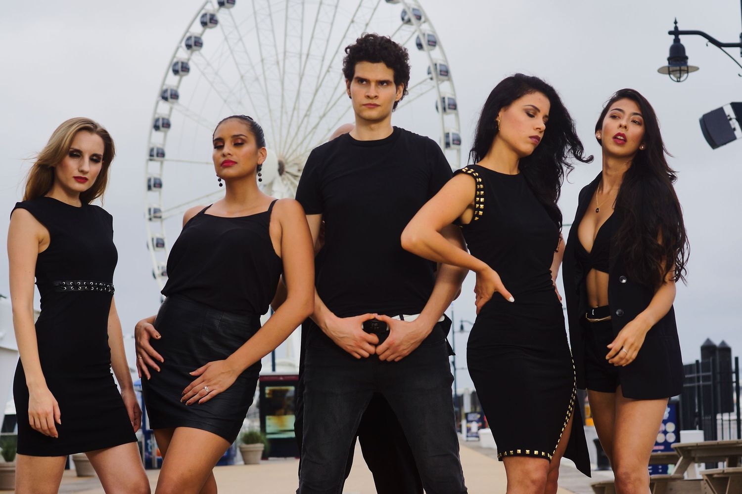 Fashion models striking poses in black outfits with ferris wheel backdrop.