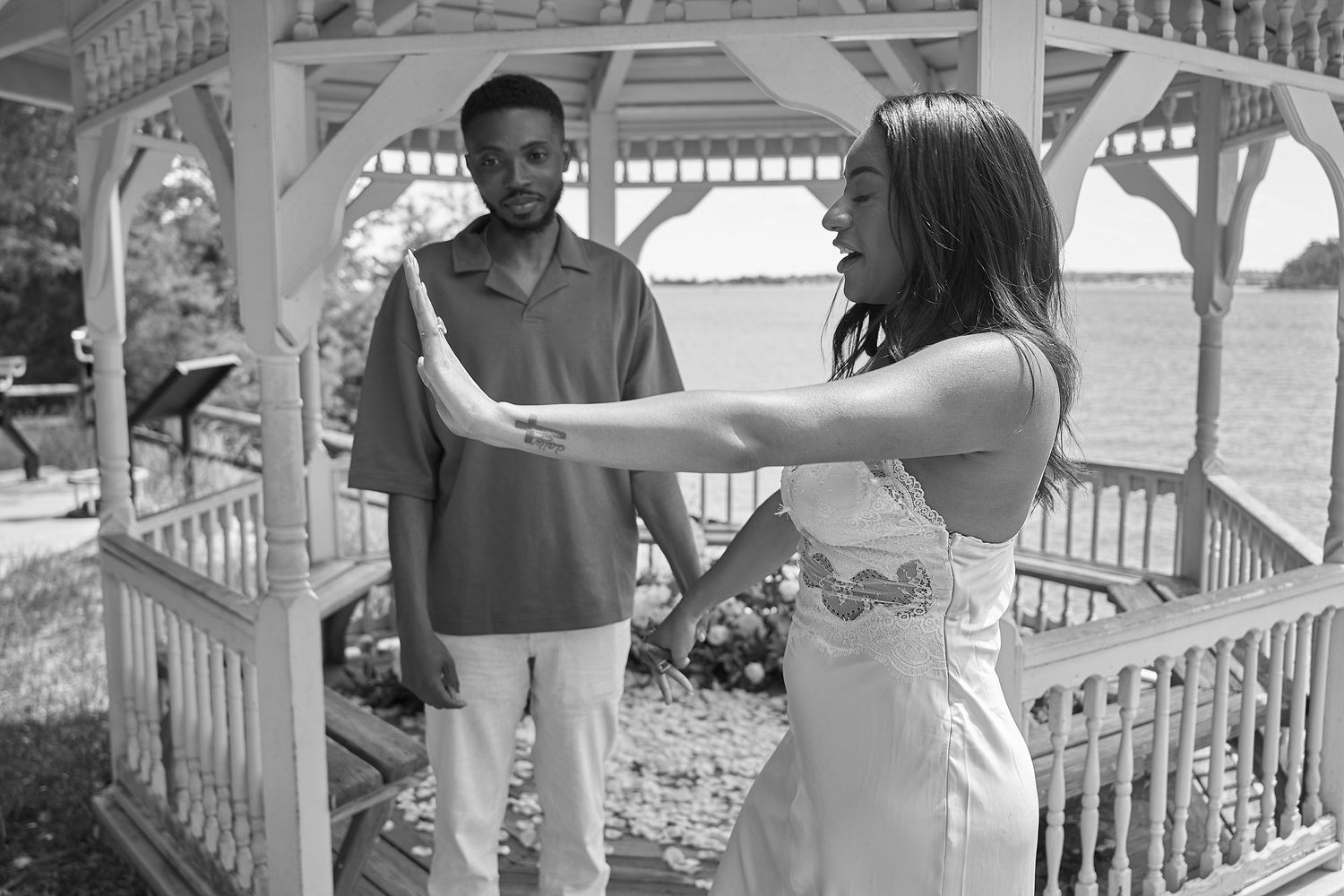 Bride and groom share a tender moment outside a white gazebo in black and white photo.