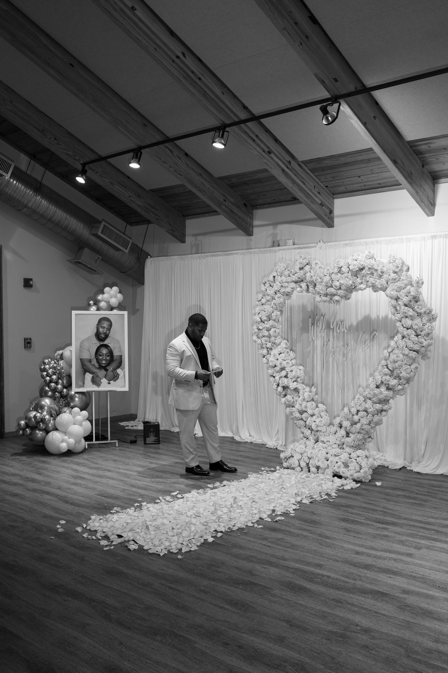 Black and white photo showing setup of curved floral arch installation in event space.