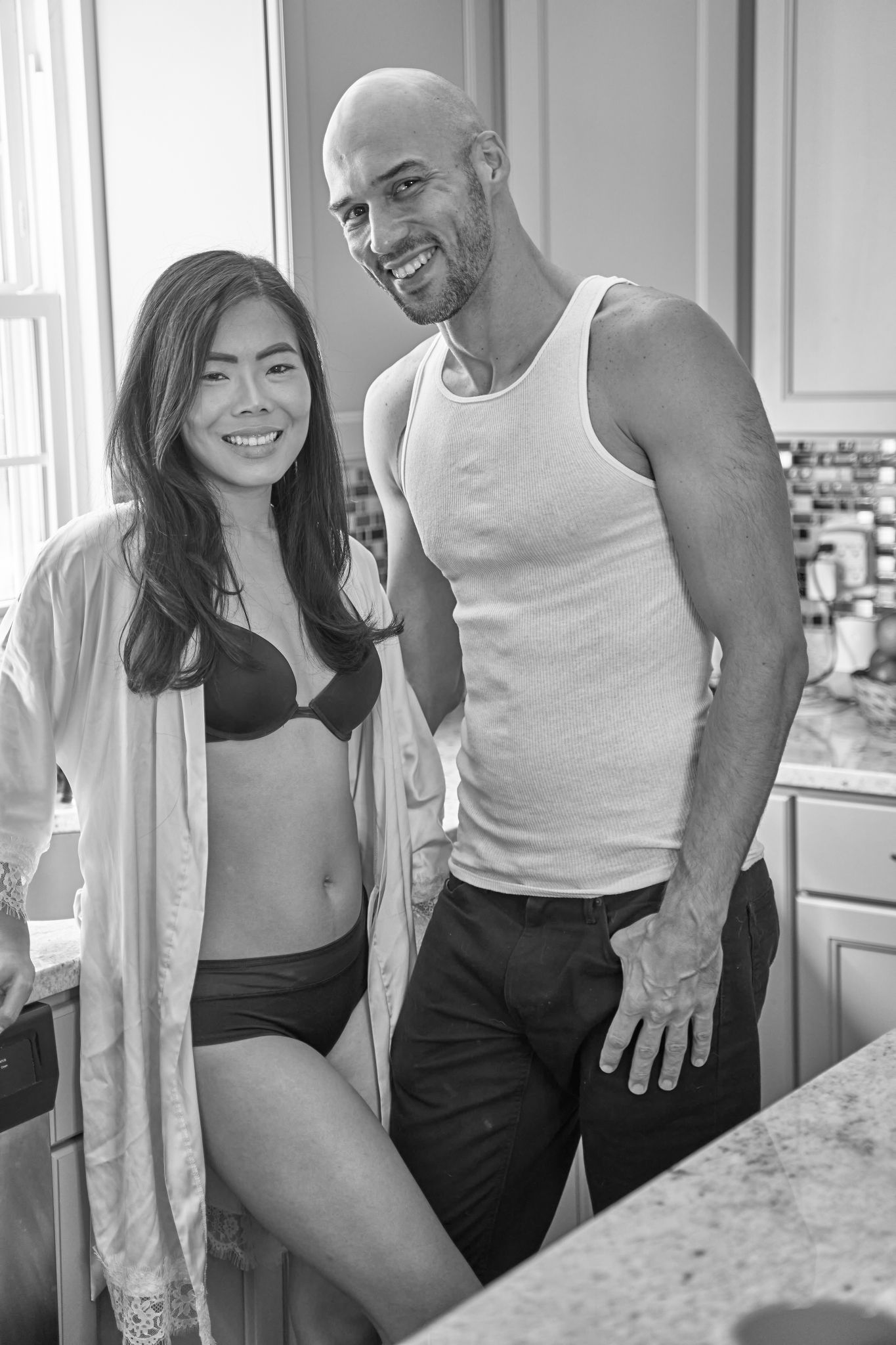 A couple poses playfully in a modern kitchen setting with black and white tones.