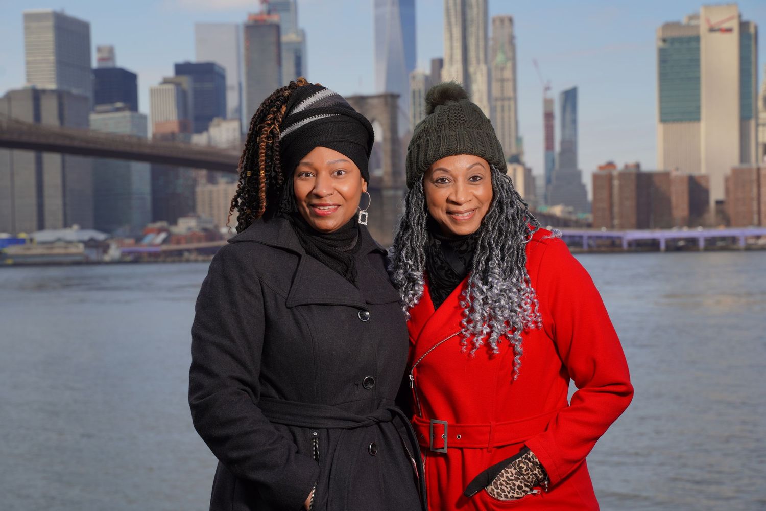 Two people posing together with NYC skyline and East River in background.