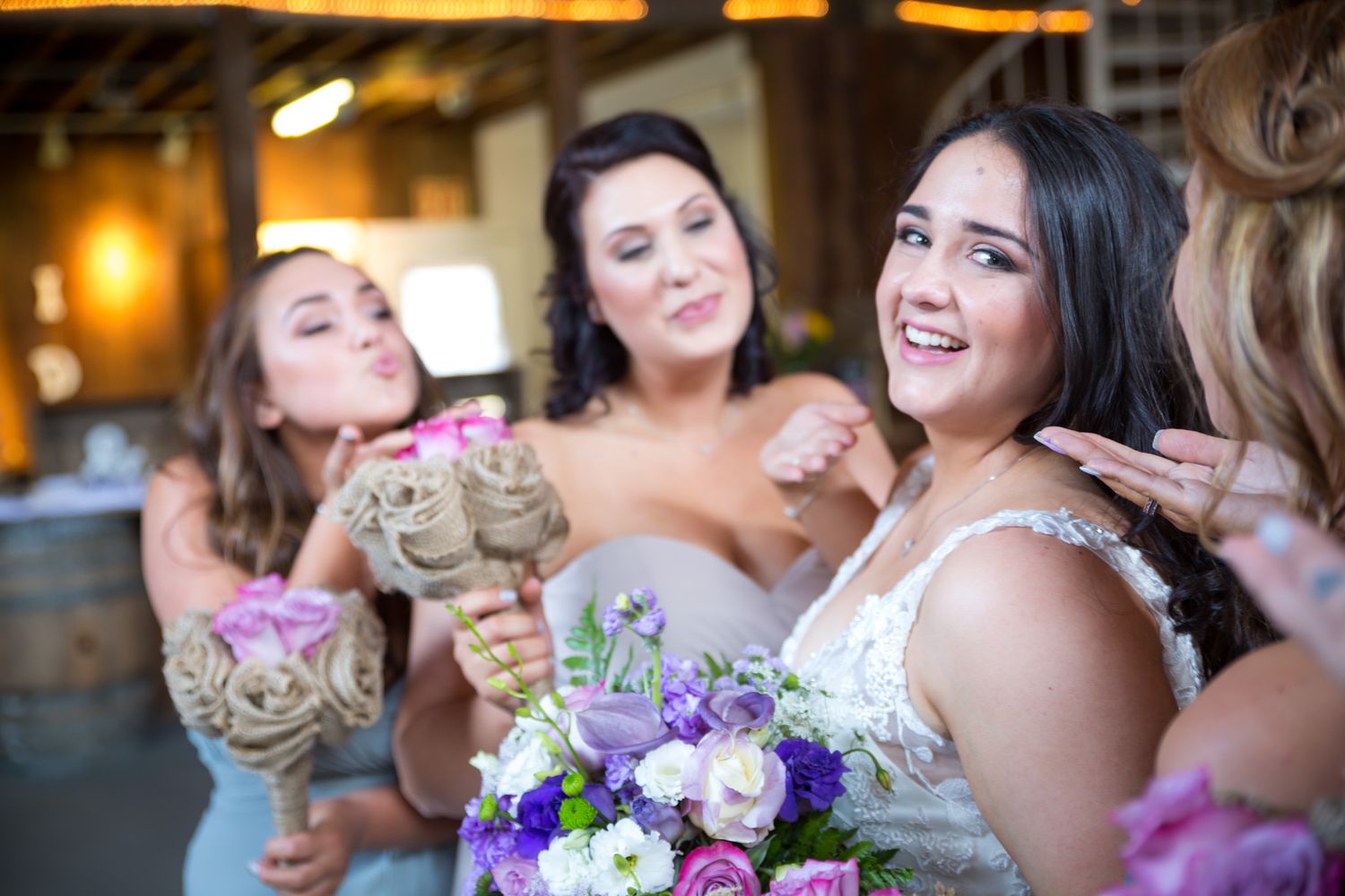Wedding party members share a joyful moment with bouquets featuring purple and pink flowers.