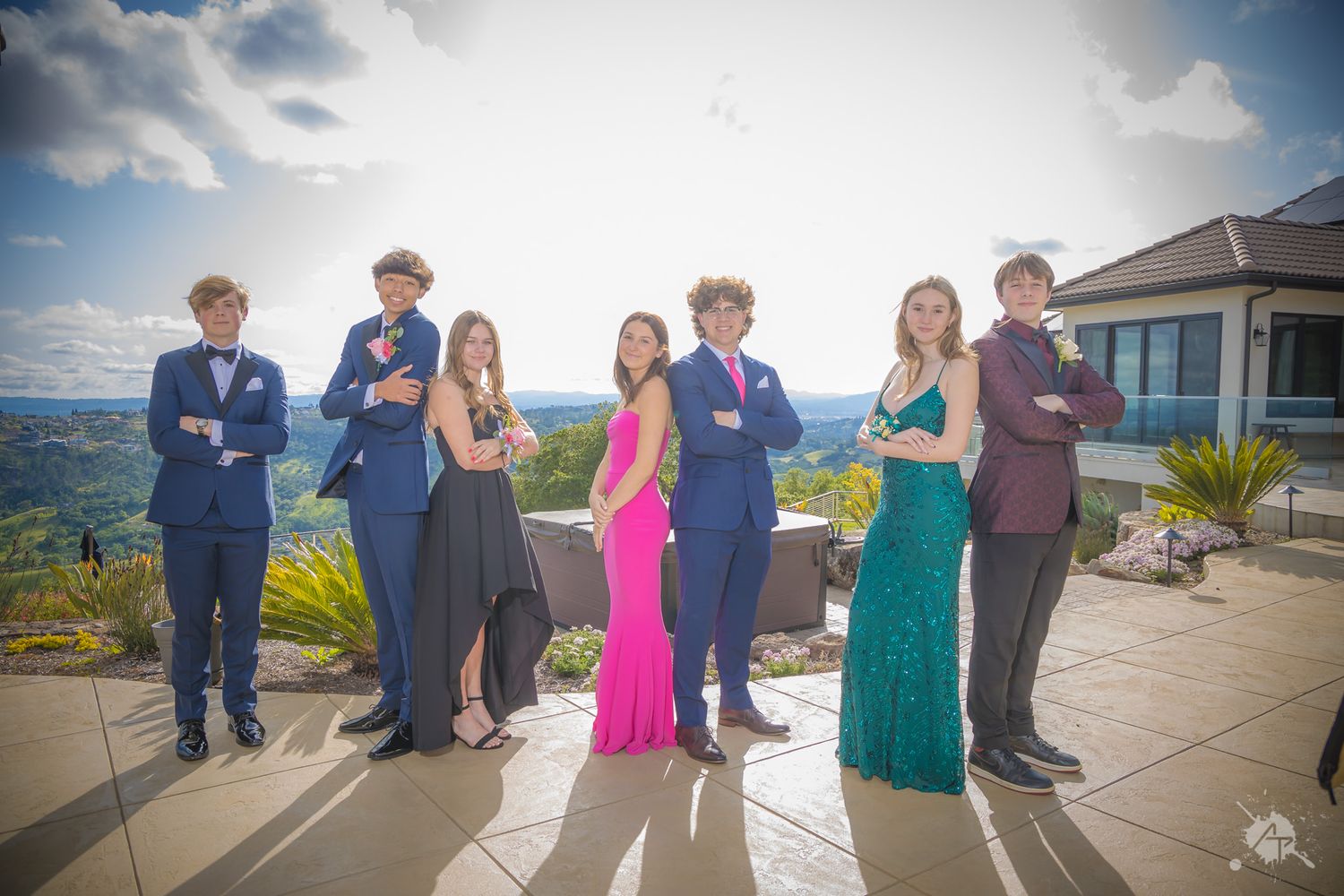 A group in formal attire poses together on a mountaintop terrace with scenic views.
