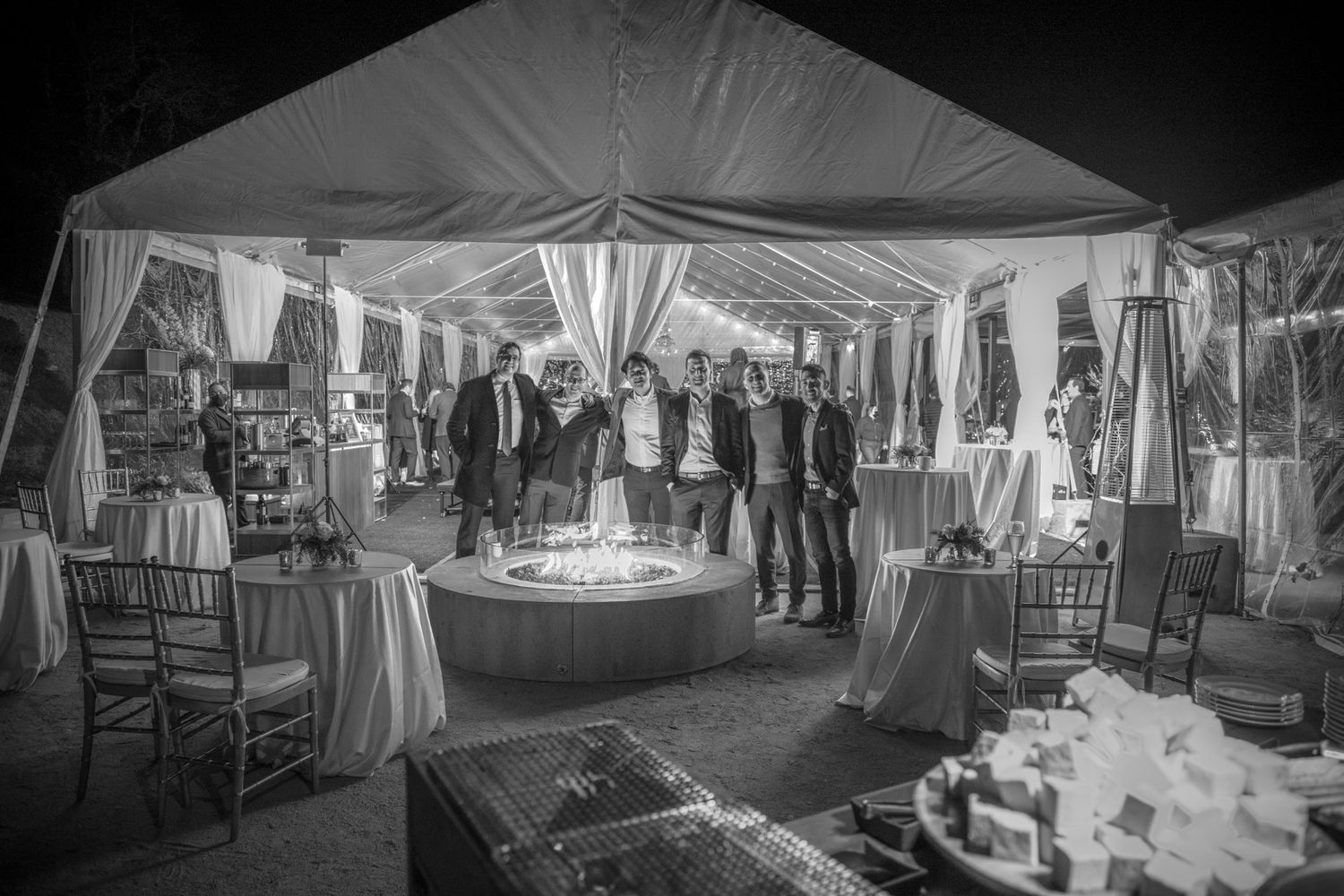 Black and white photo of elegant draped wedding reception tent with tables and lighting.
