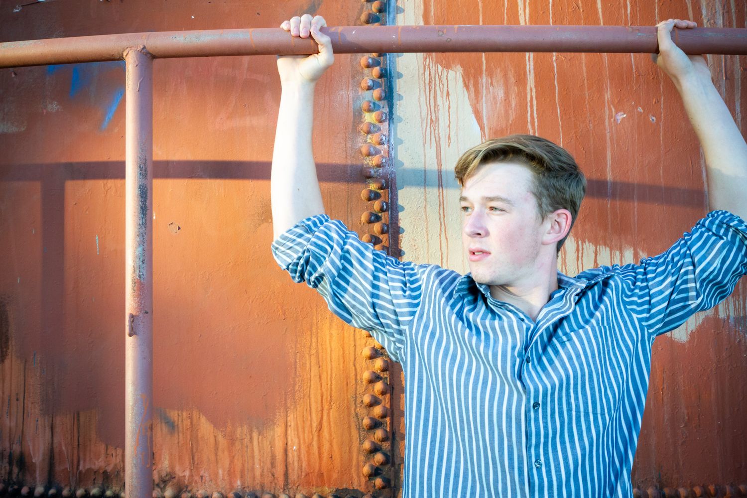 Portrait against rustic orange wall with raised arms on metal bars.