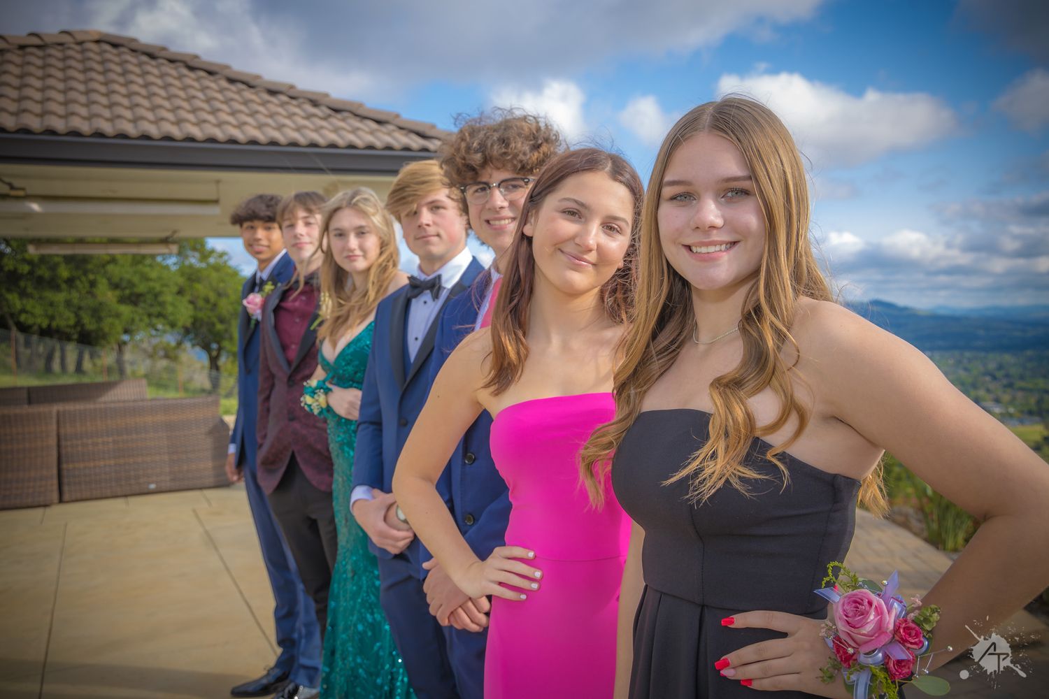 Friends in formal attire pose together for a group photo against mountain scenery.