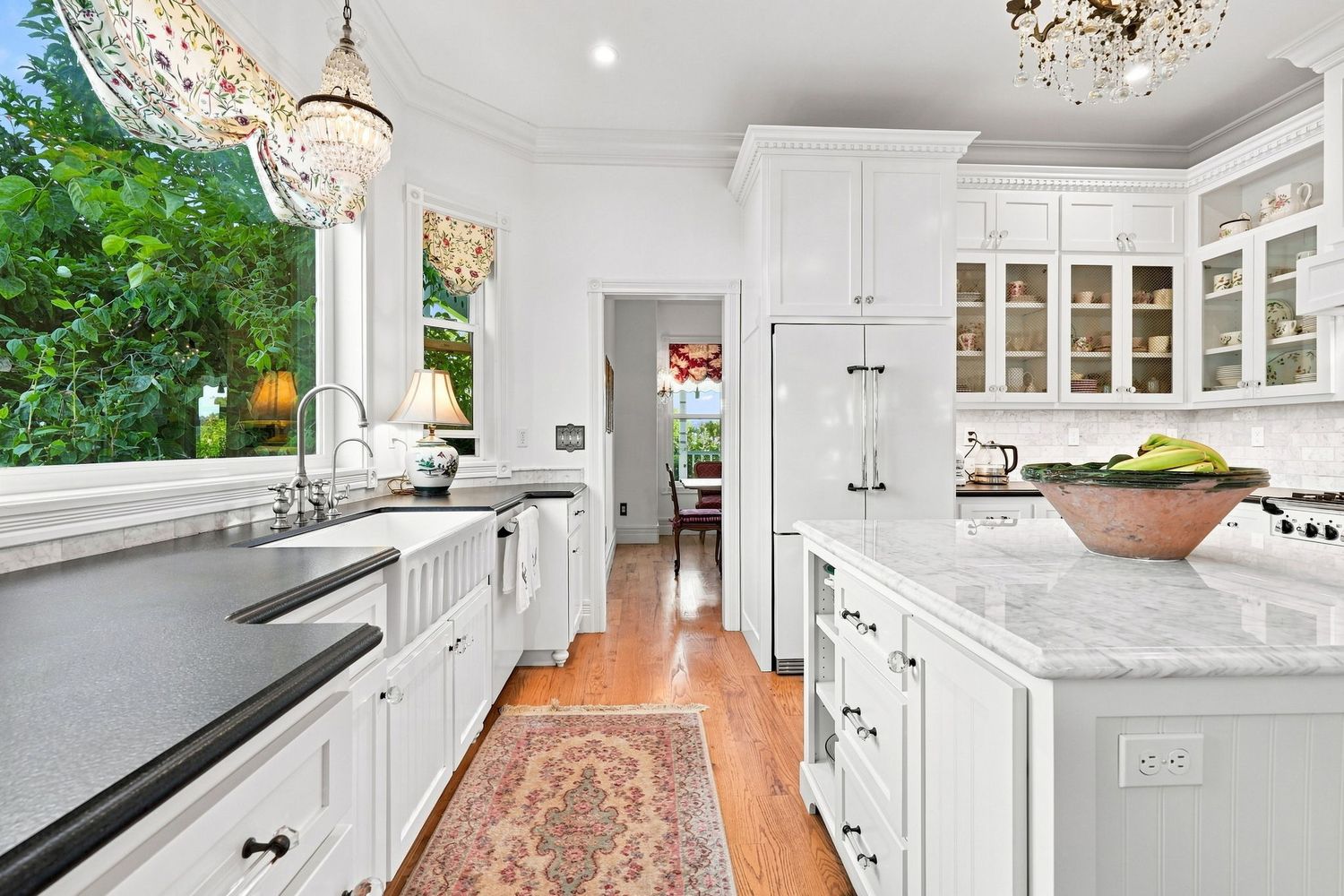 Elegant white kitchen with marble countertops, glass-front cabinets, hardwood floors, and crystal chandeliers.