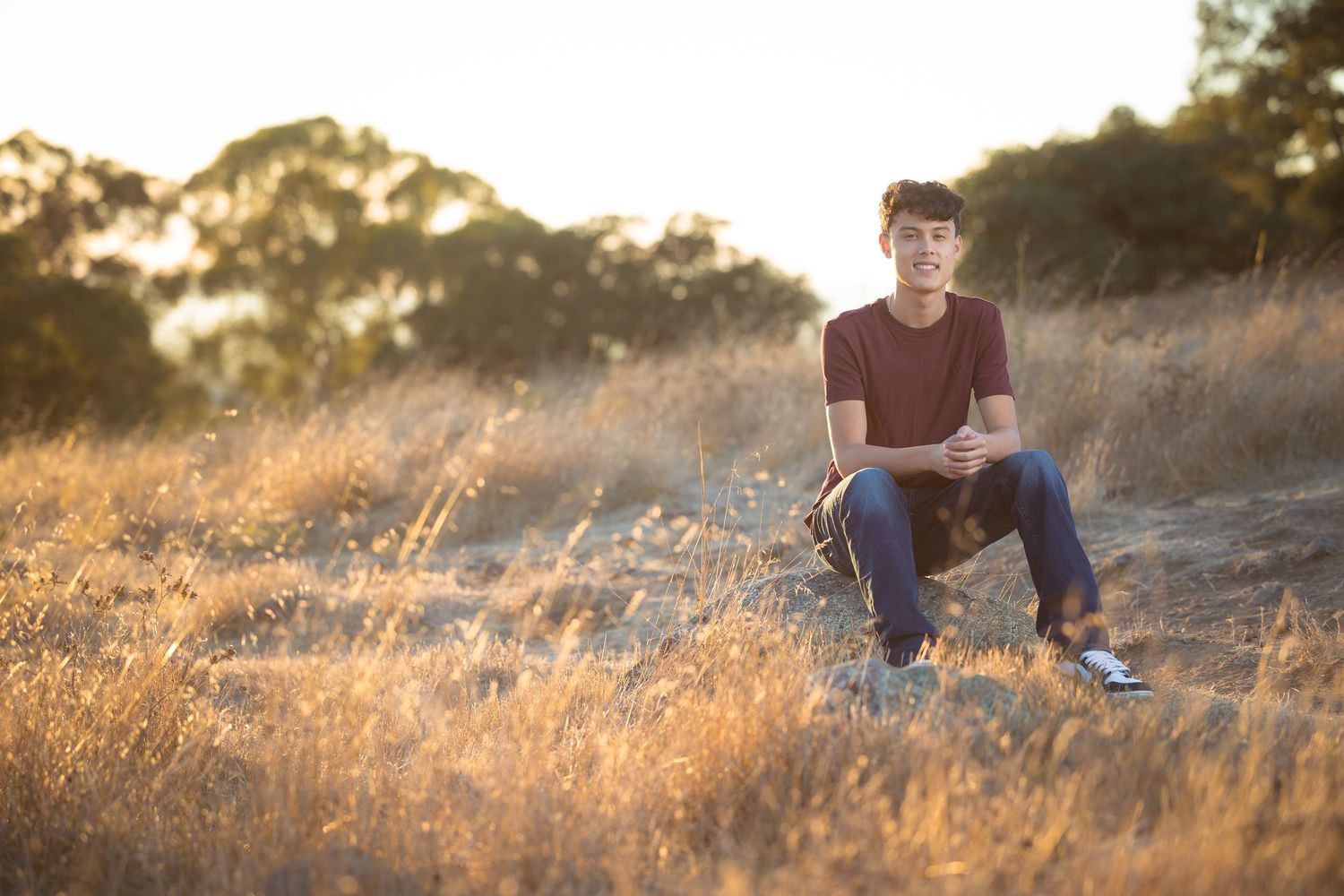 Person in casual attire seated on hillside during golden hour.