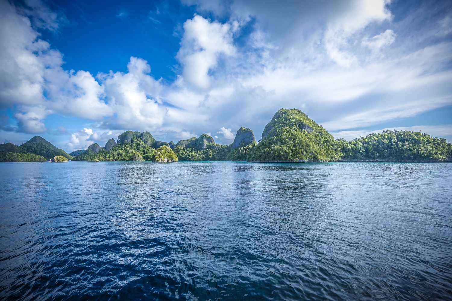 Dramatic limestone karst islands rise from turquoise waters under cloudy skies in a tropical paradise.