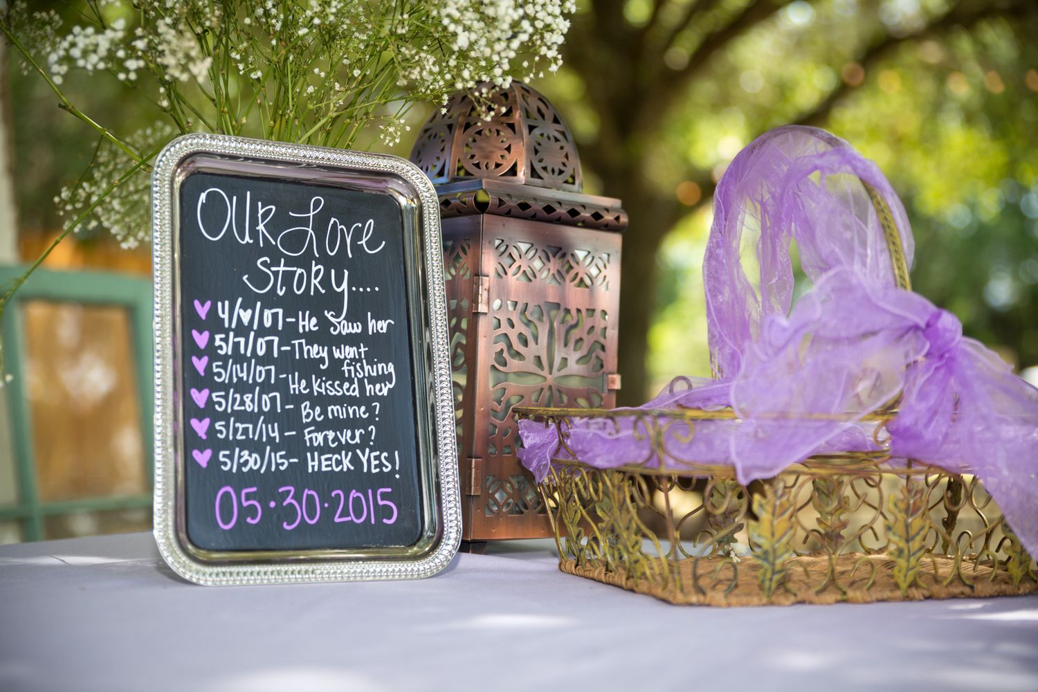Vintage style wedding decor featuring a chalkboard menu sign, decorative lantern and purple tulle accent on outdoor table.