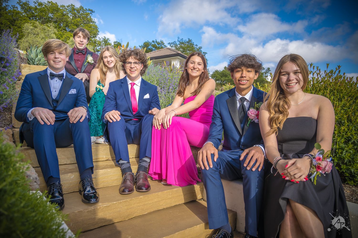 Group in formal attire seated on wooden bench with mountain landscape in background.