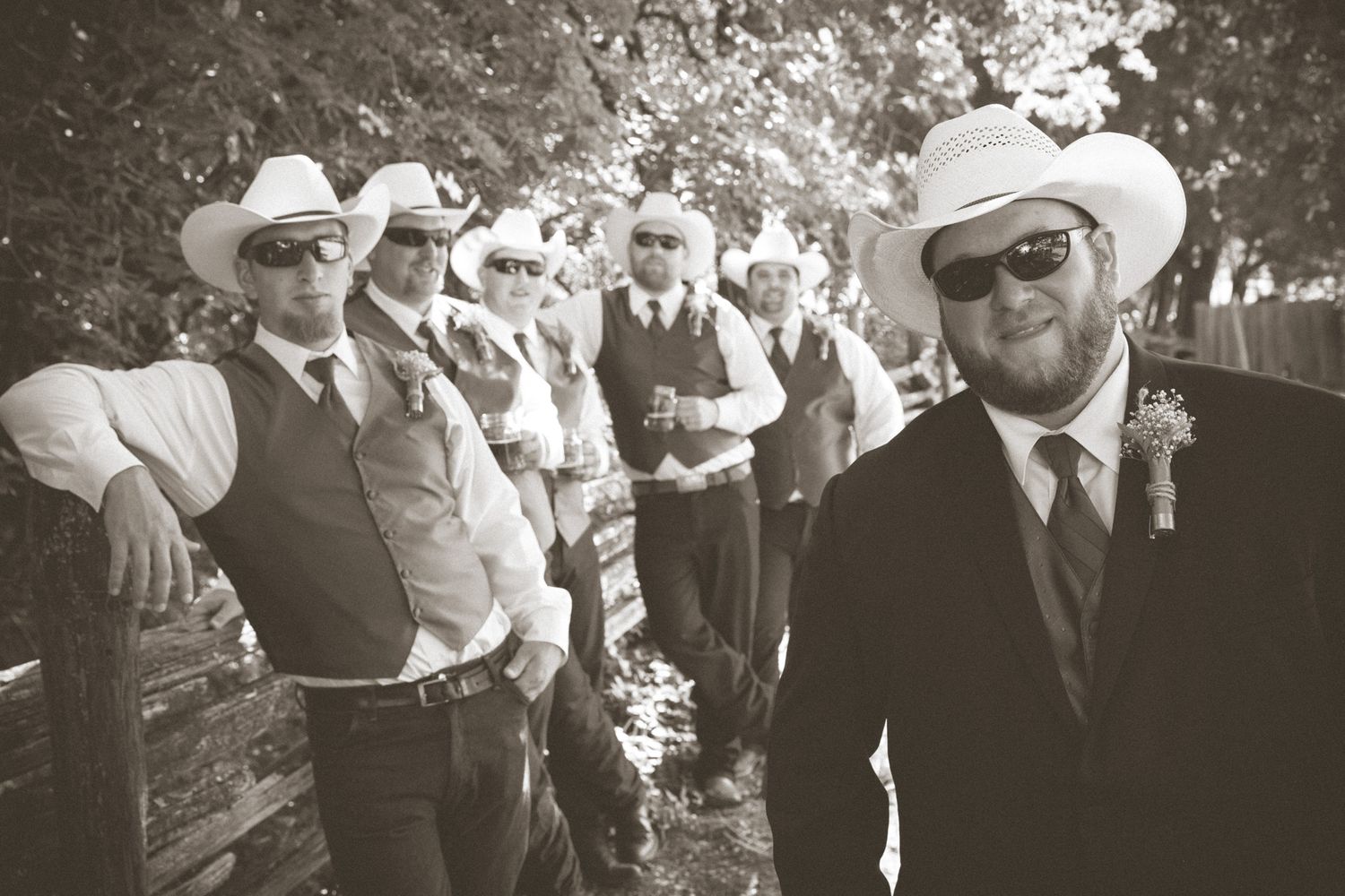 Wedding party members in cowboy hats and formal attire pose together in black and white.