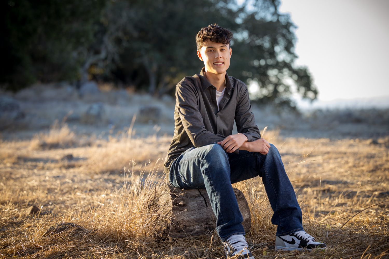 Senior Photos - Portrait of a casual figure seated on a rock during golden hour in a natural outdoor setting.