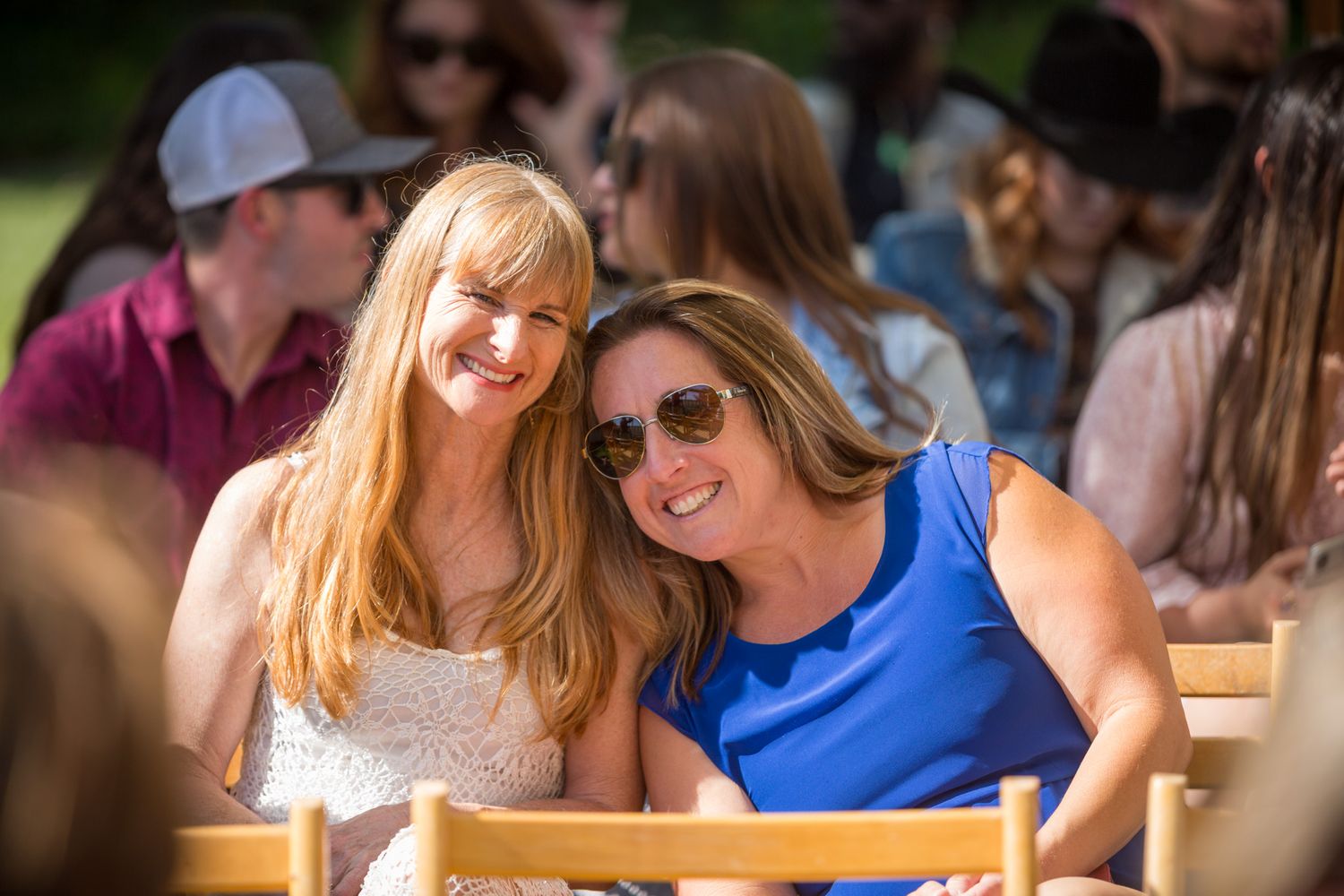 Wedding guests in summer attire smile while seated at an outdoor ceremony.