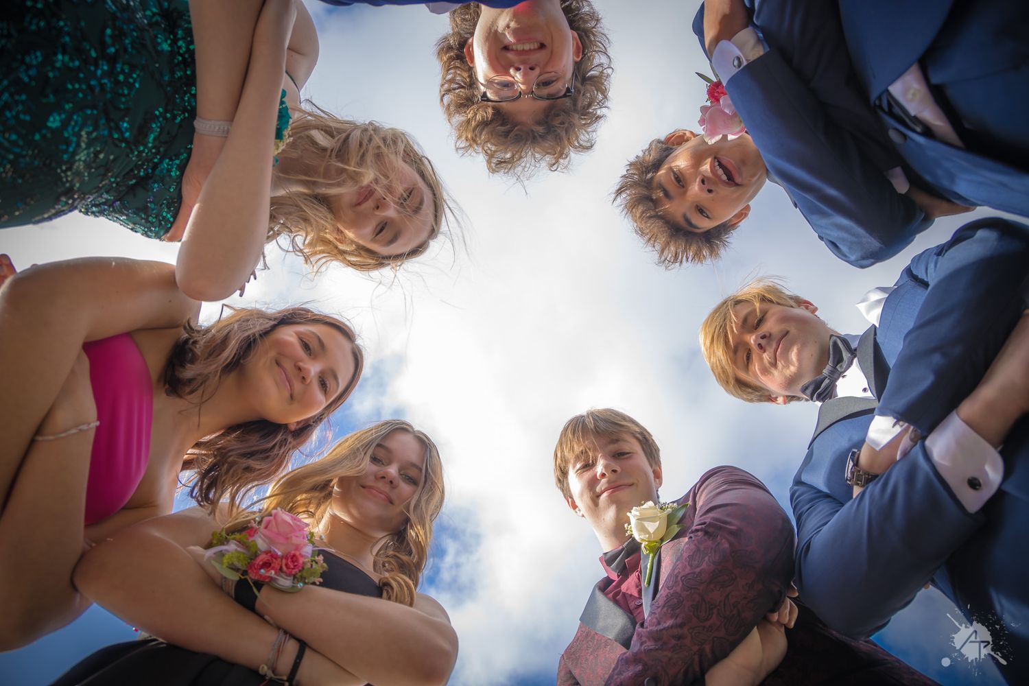 Looking up at a circle of friends in formal wear against a bright sky.