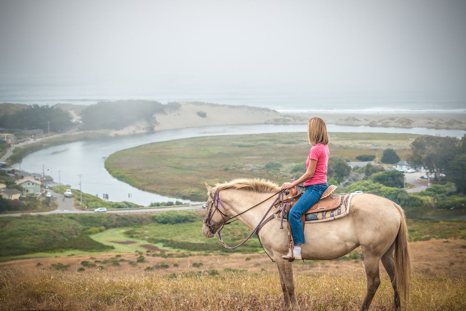 Horse rider overlooking scenic river valley from hilltop viewpoint.