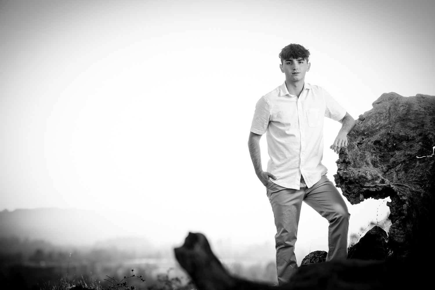 Black and white portrait of person in button-down shirt standing on mountain overlook.