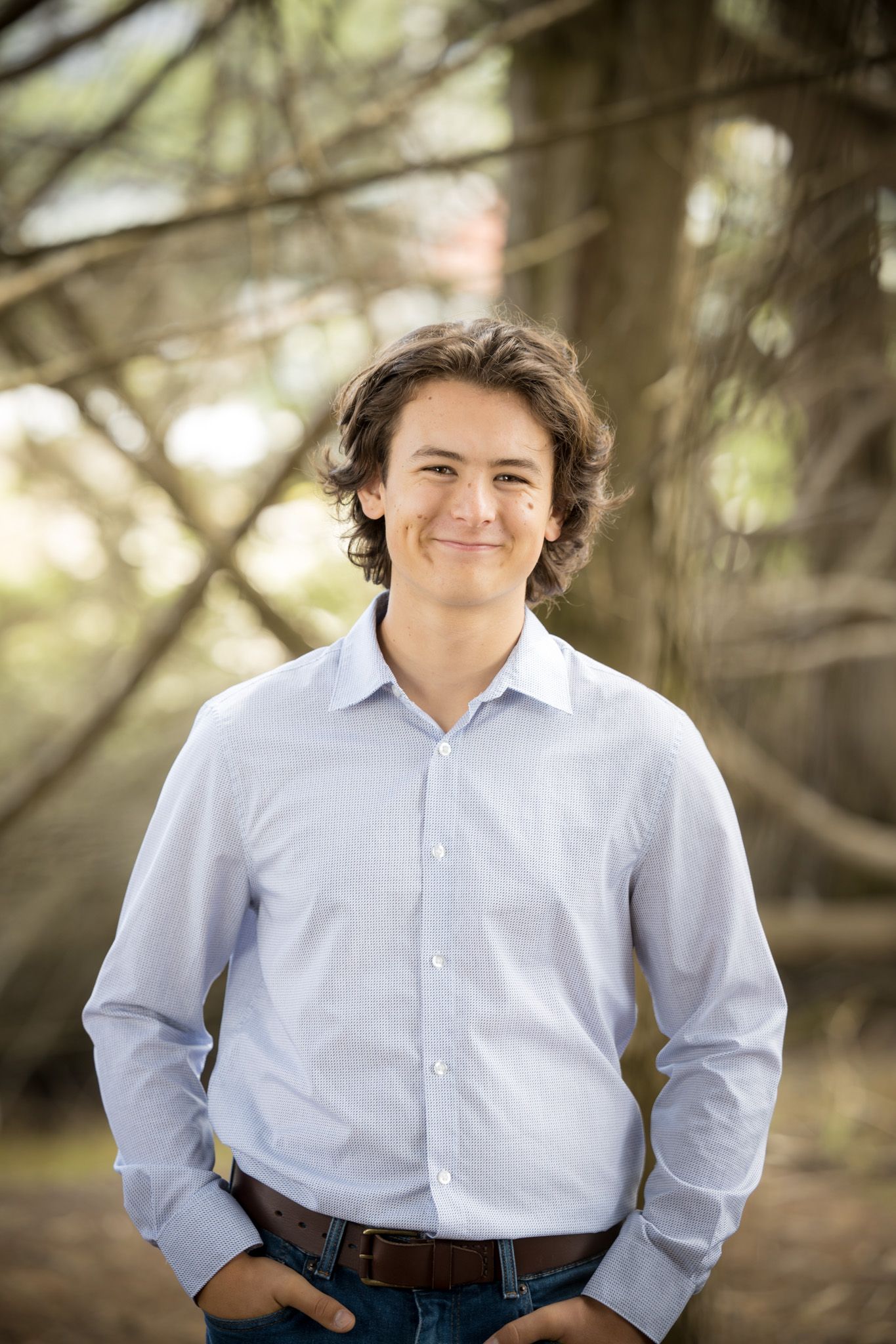 Portrait in light blue dress shirt against natural wooded background.