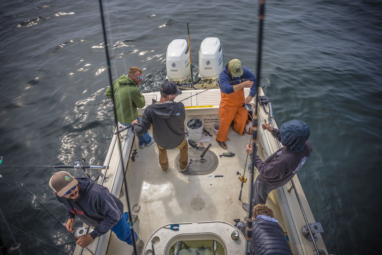 Aerial view of people fishing from the back of a boat on sparkling blue water with fishing rods and equipment.