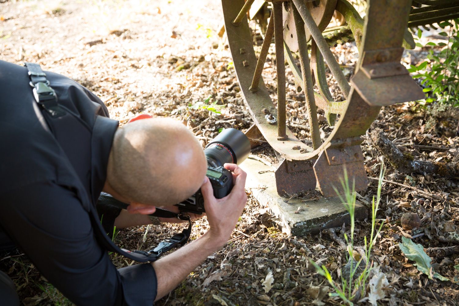 A photographer lies on the ground capturing a low-angle shot of a vintage bicycle wheel in autumn leaves.