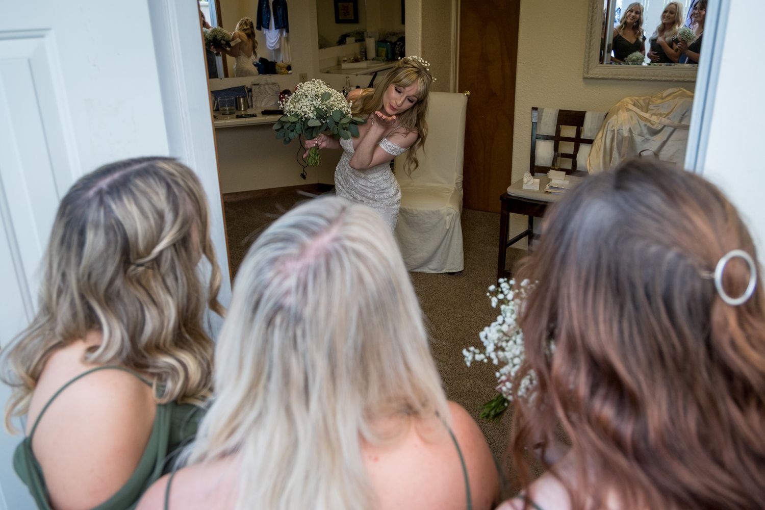 Bridesmaids with blonde and brown hair gathered around a mirror for wedding preparations.