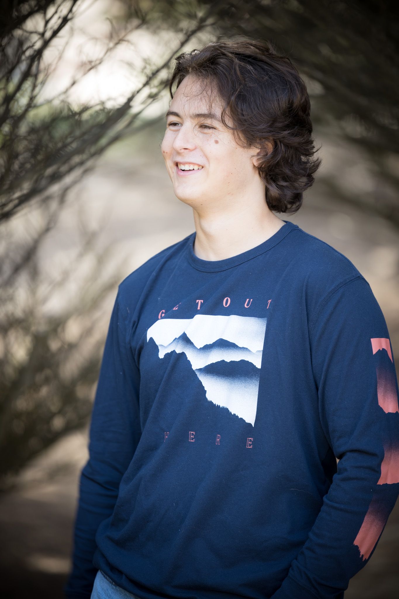 Outdoor portrait series featuring navy mountain graphic sweatshirt against natural backdrop.