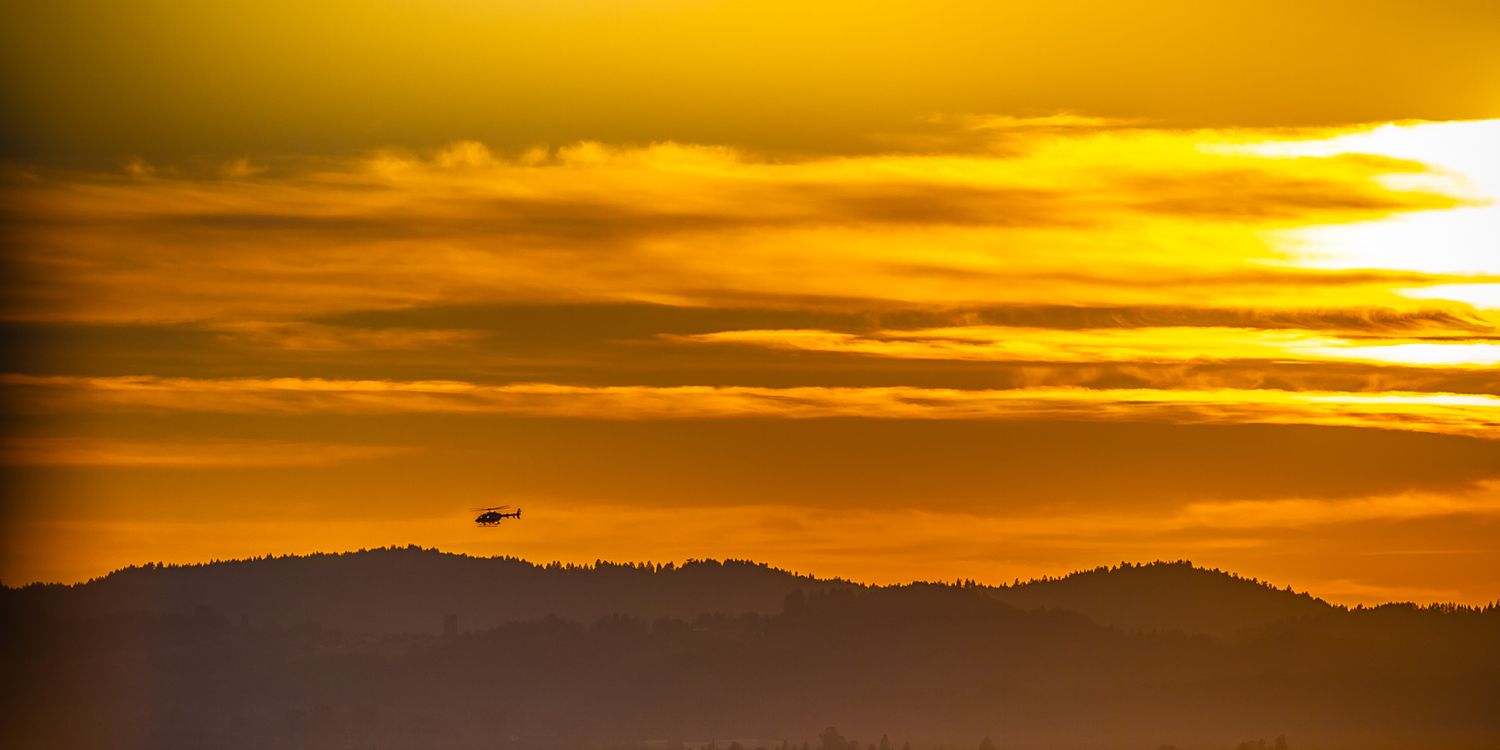 A small aircraft silhouetted against dramatic golden sunset sky over mountain ridges.