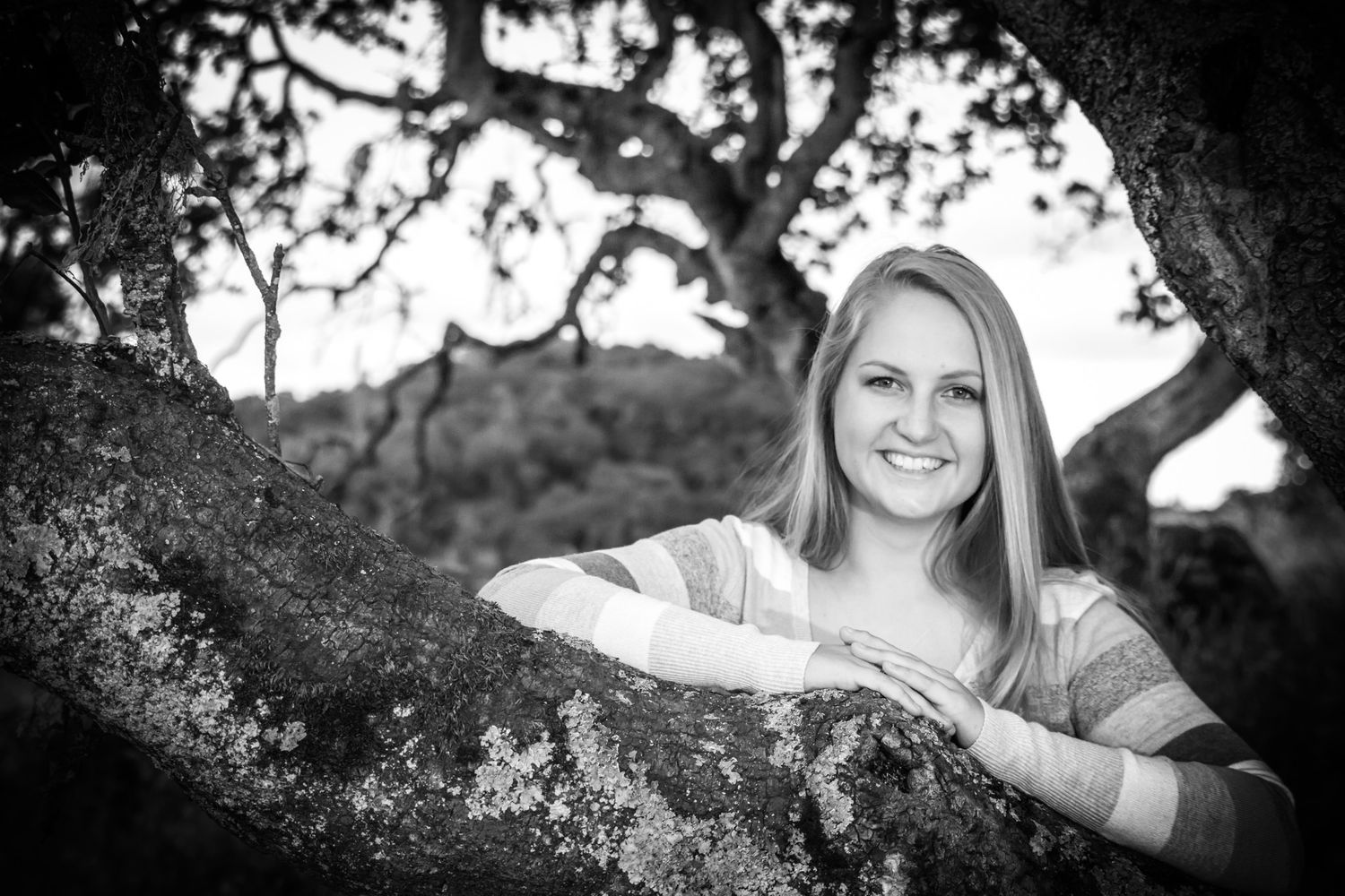 Black and white portrait of a person lounging on a tree branch in a casual outdoor setting.