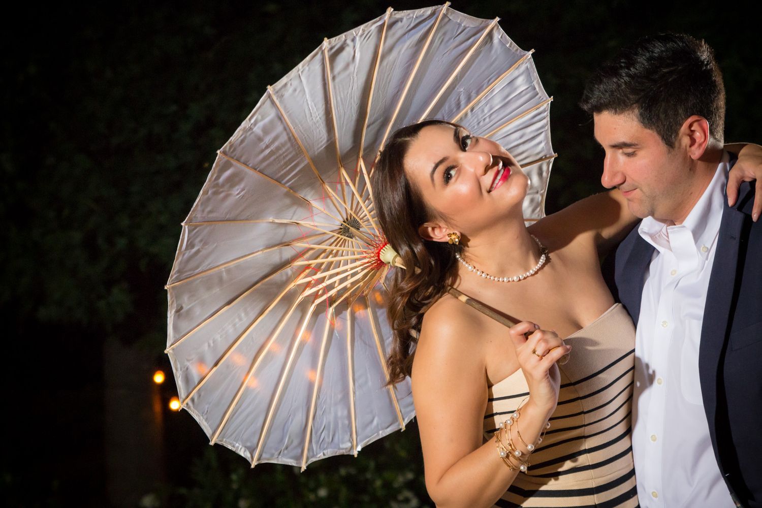 Elegant couple poses with decorative parasol at nighttime celebration.