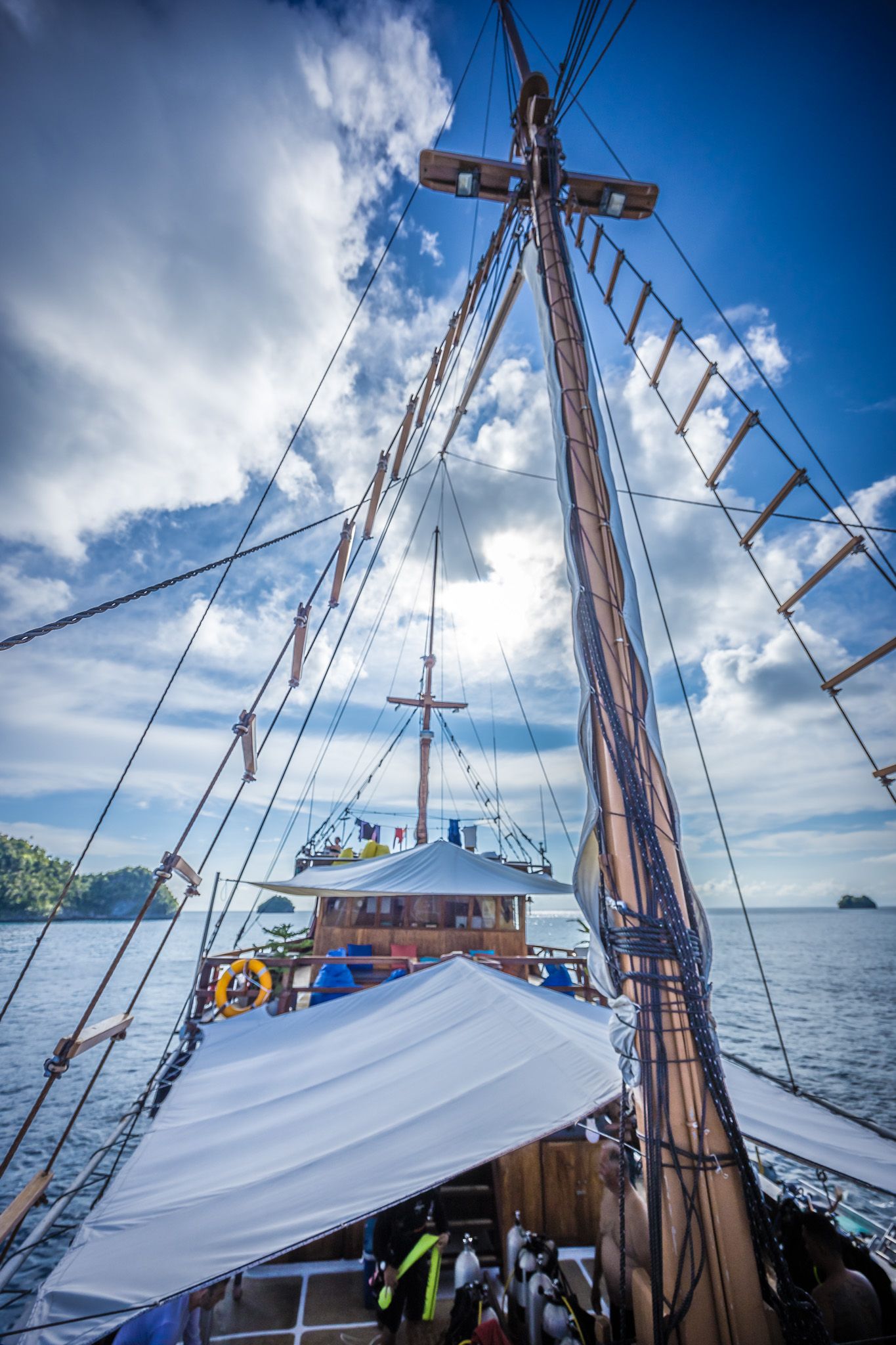 View of sailboat masts and rigging against bright blue sky with white clouds.