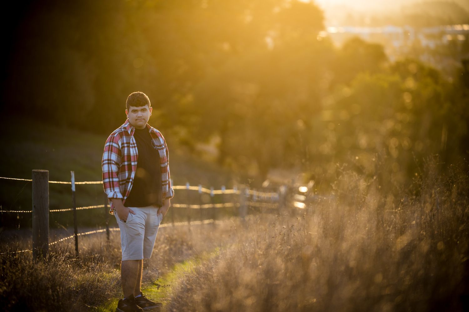 Senior Photos - Figure silhouetted against golden sunset near rustic fence in countryside setting.