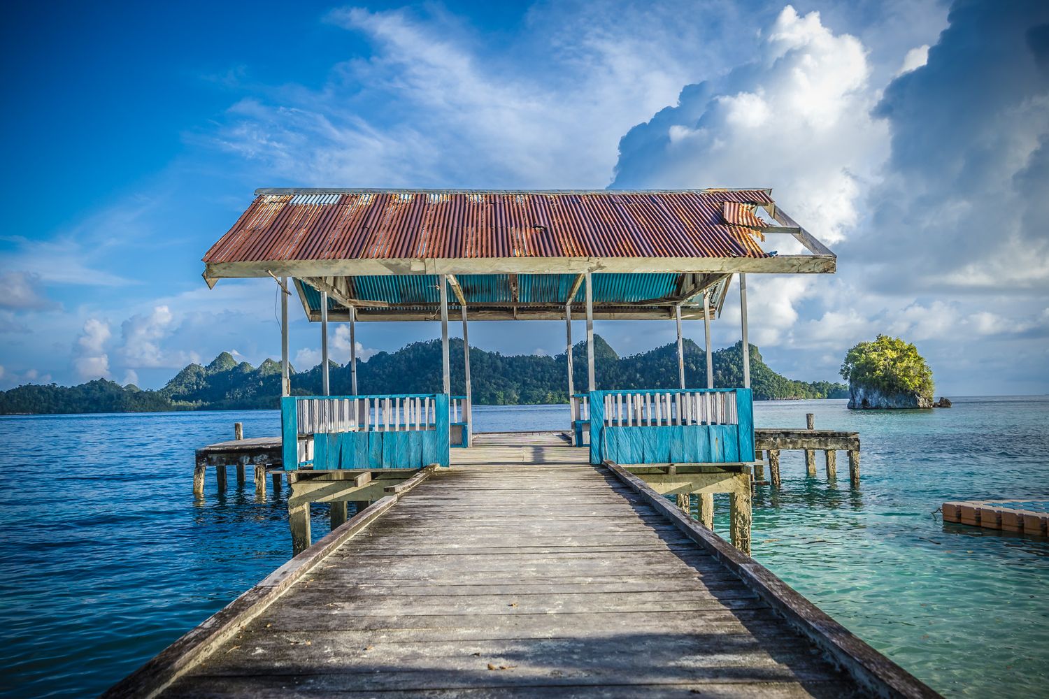 Wooden pier with covered pavilion extends over crystal clear tropical waters.
