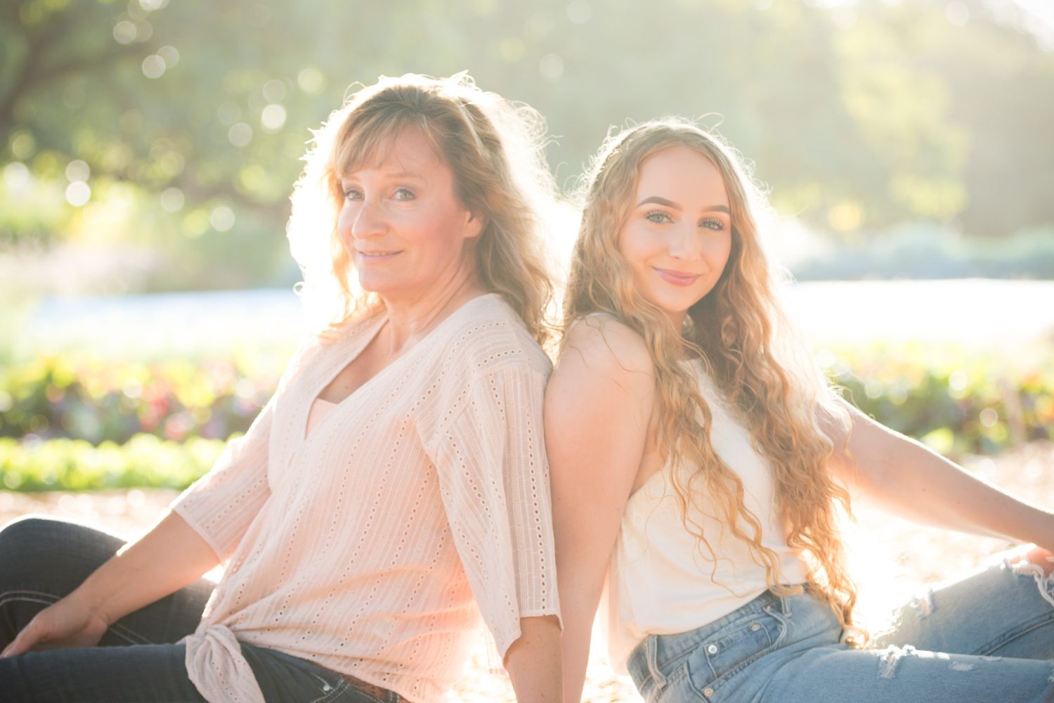 Two figures sit back-to-back outdoors during sunset with golden light illuminating their profiles.