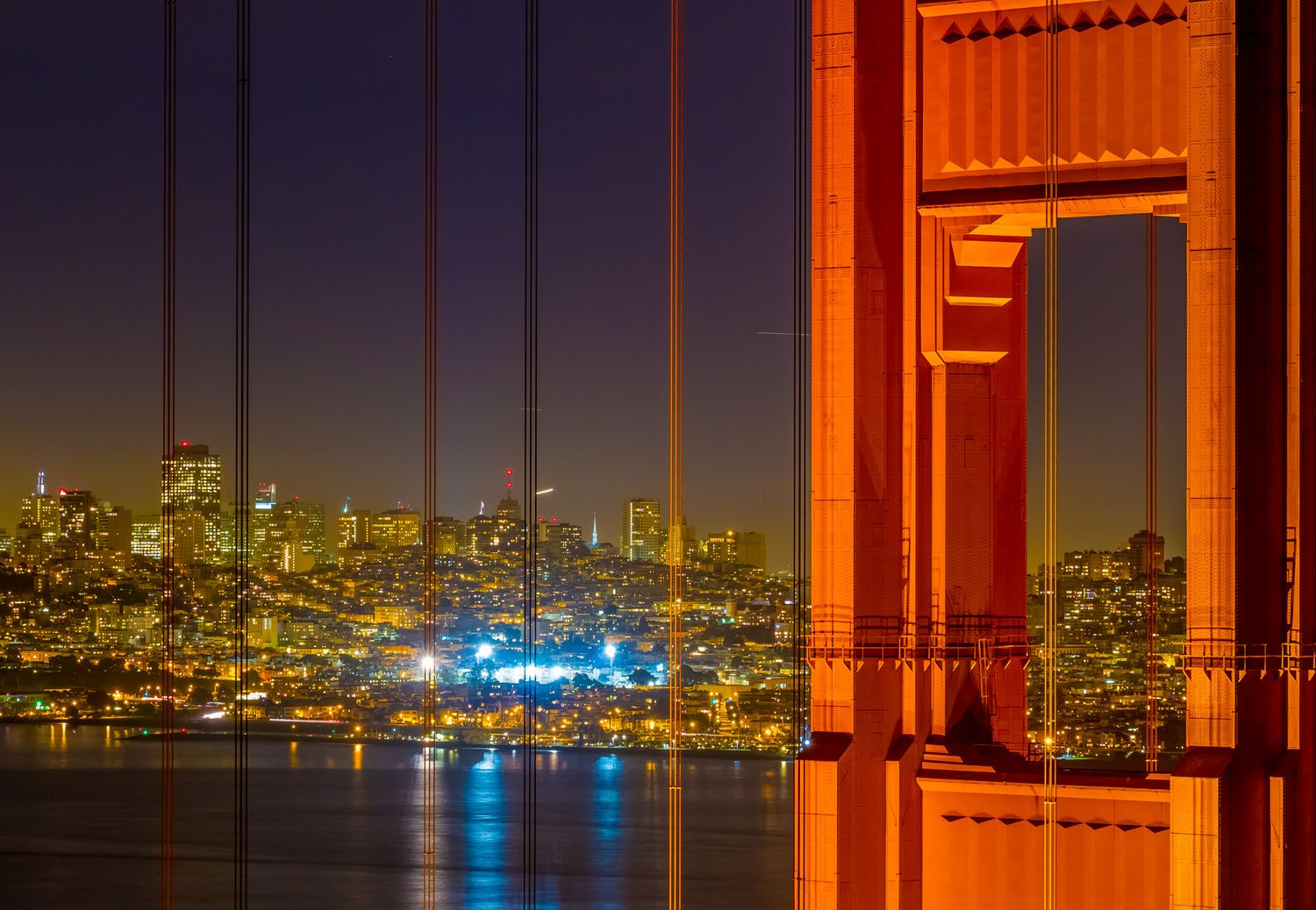 San Francisco skyline and bay viewed through Golden Gate Bridge tower at twilight.