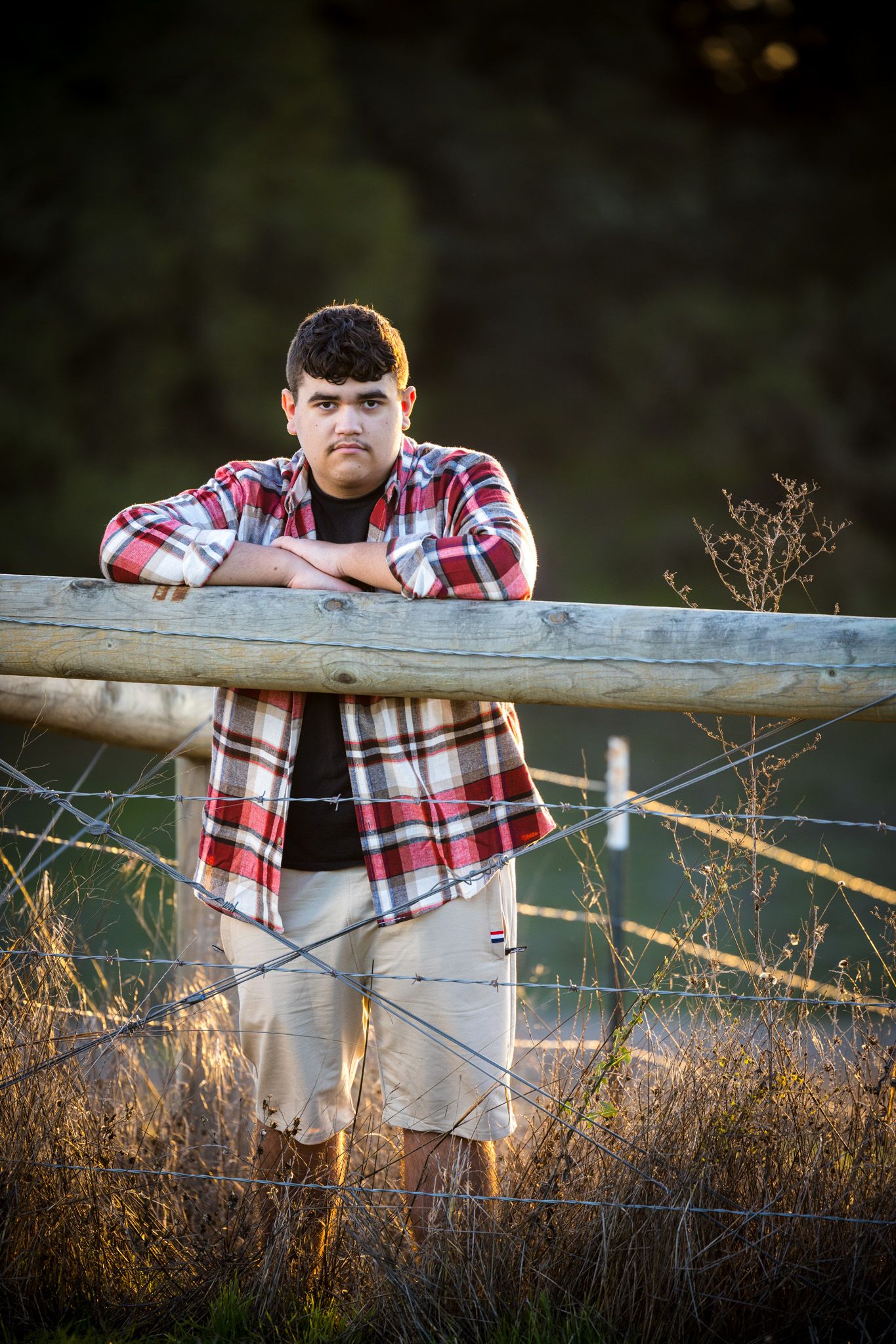 Senior Photos - Portrait at rustic wooden fence during golden hour with dried grass in foreground.