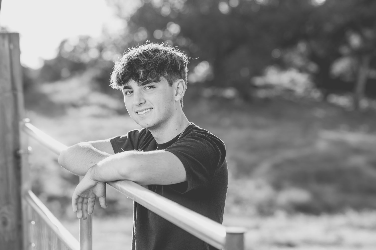 Black and white portrait of someone leaning on wooden railing with dreamy expression.